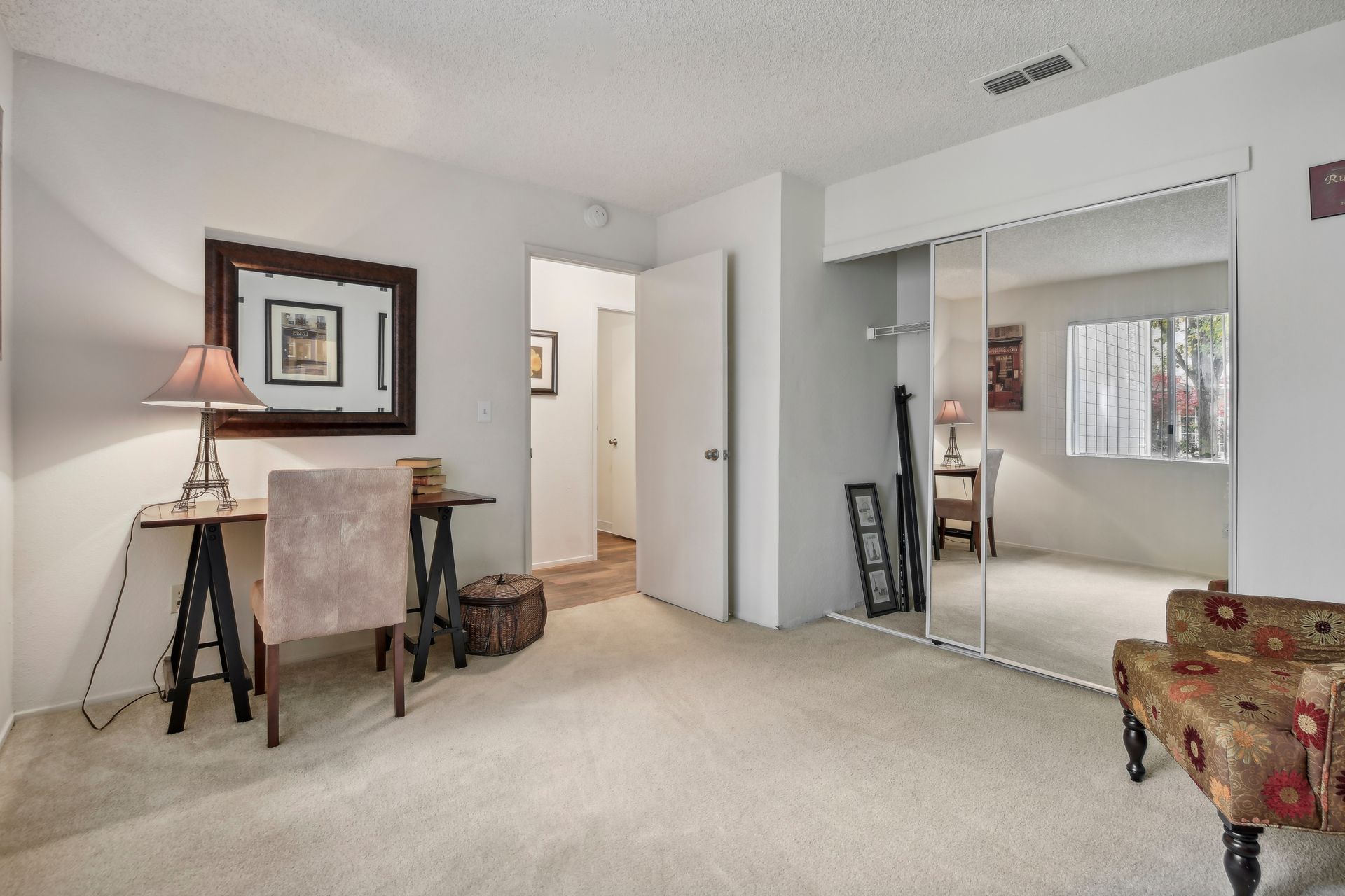 Bedroom with a desk, chair, mirror, and closet. Soft carpet and neutral-colored walls.