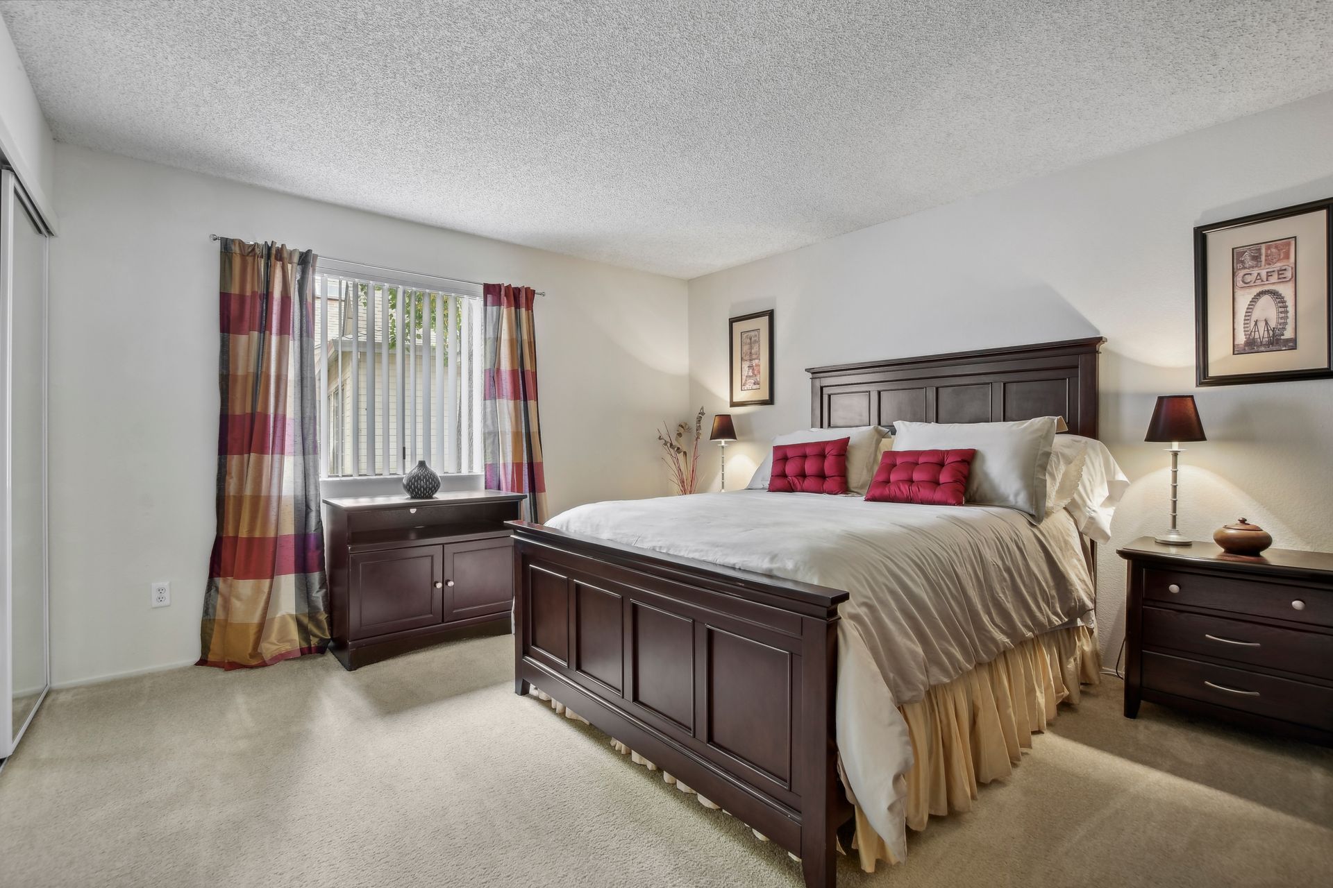 Bedroom with a dark wooden bed, dressers, patterned curtains, and lamps.