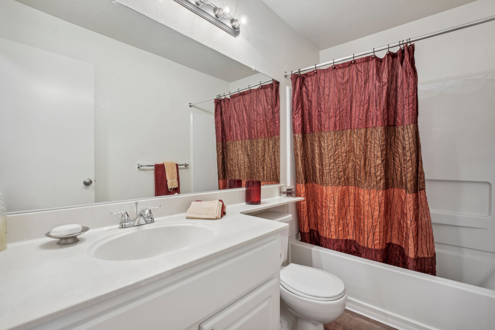 Bathroom with white sink, toilet, and bathtub with a patterned red shower curtain.
