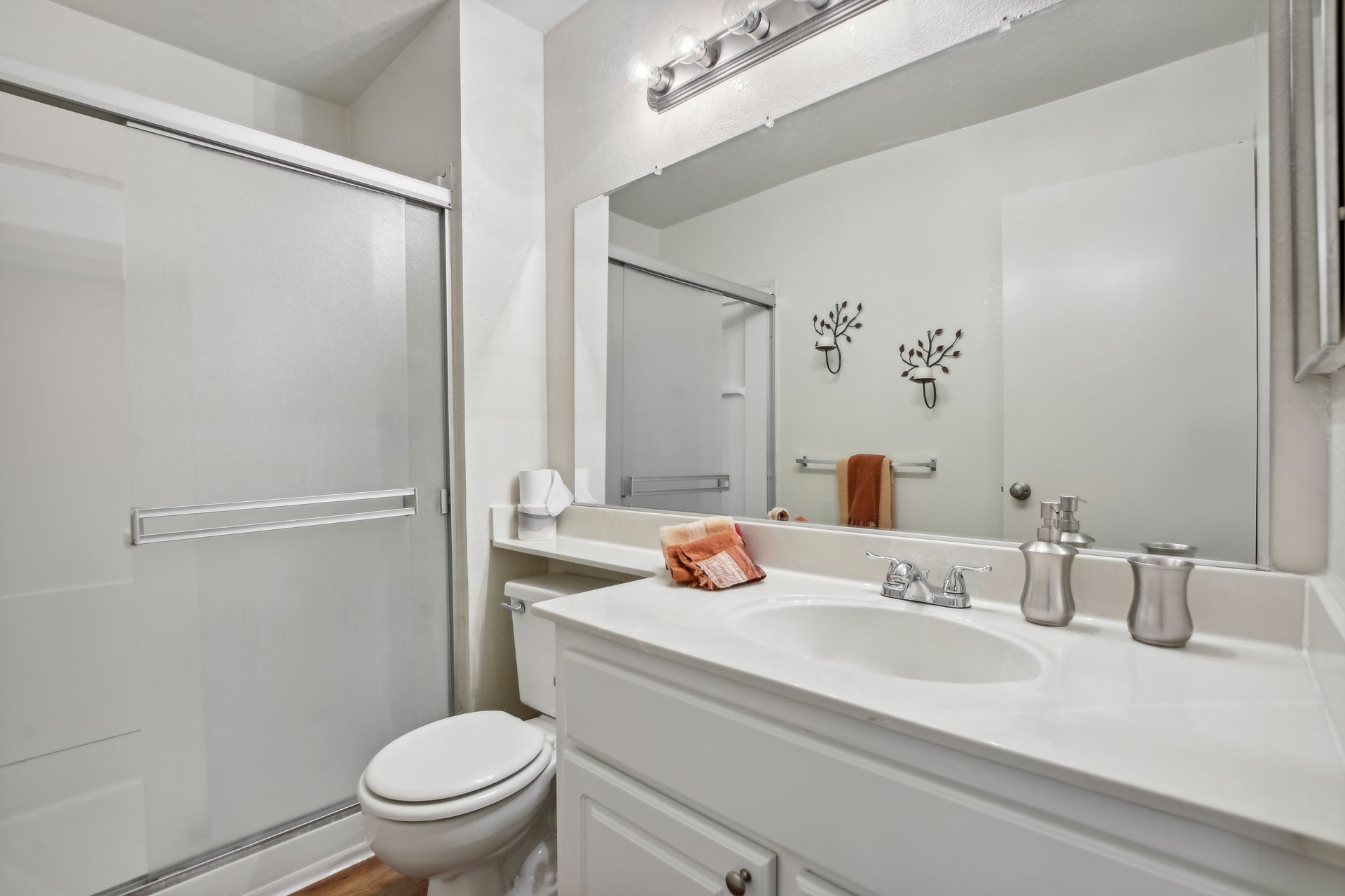 Bathroom with white fixtures, a vanity, a shower, and a large mirror.