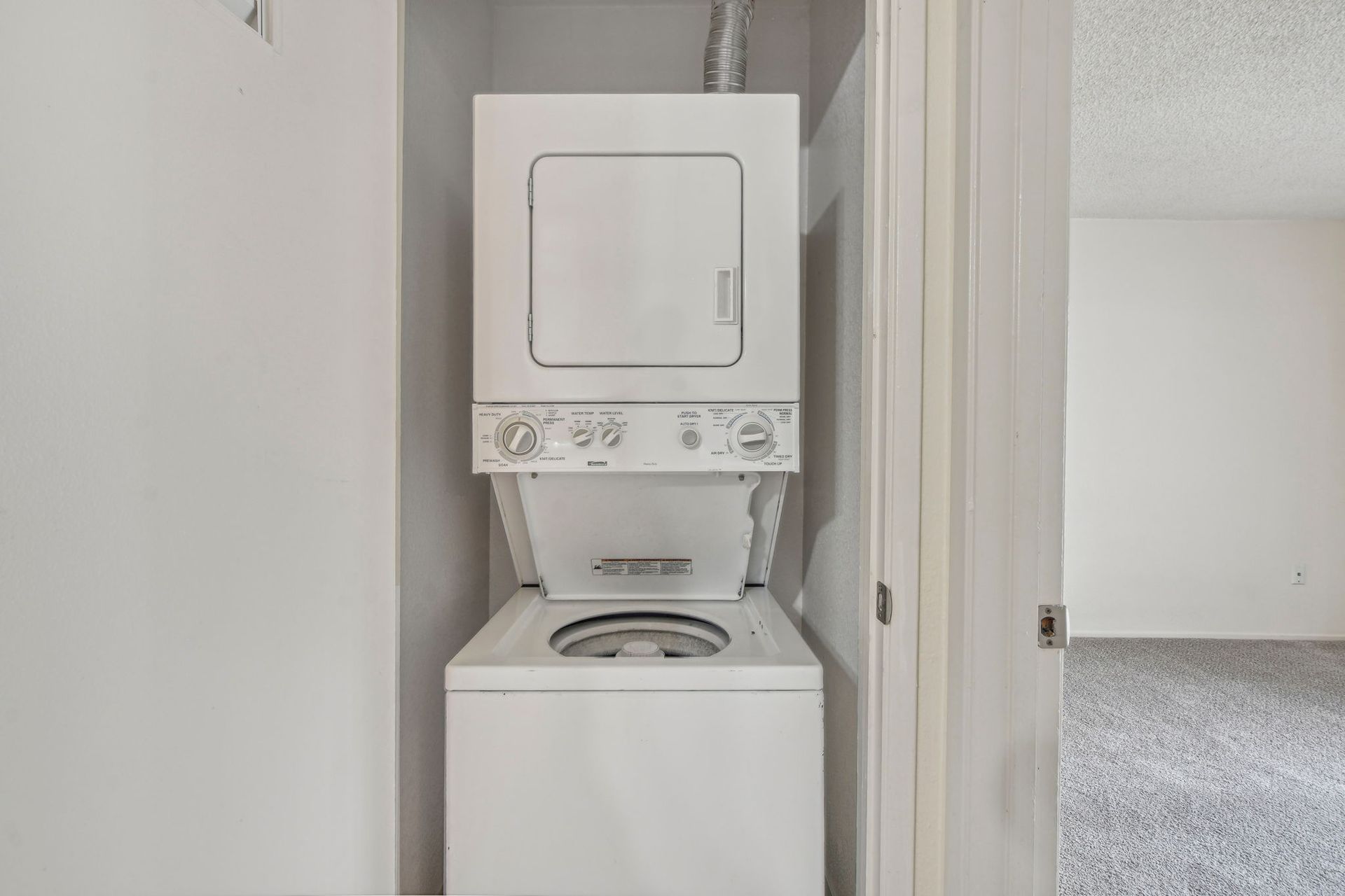 Stacked white washer and dryer in a white alcove.