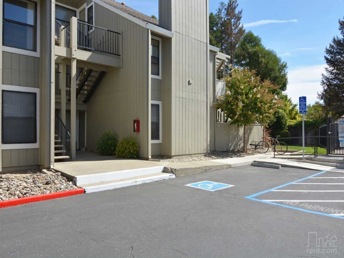 Apartment building exterior with stairs, parking spaces, and accessible parking sign.