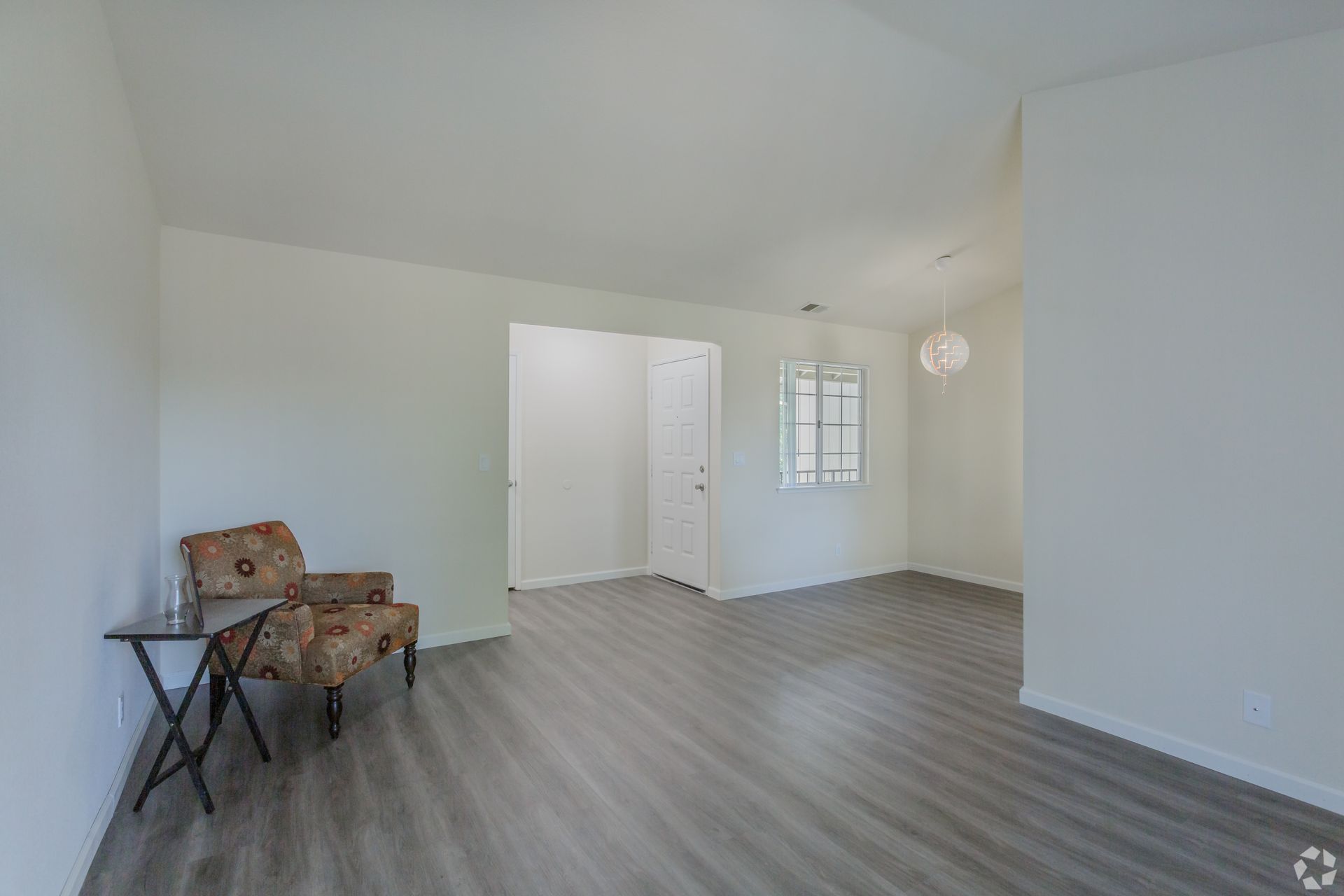 Empty living room with wood flooring, white walls, armchair, and entry door.