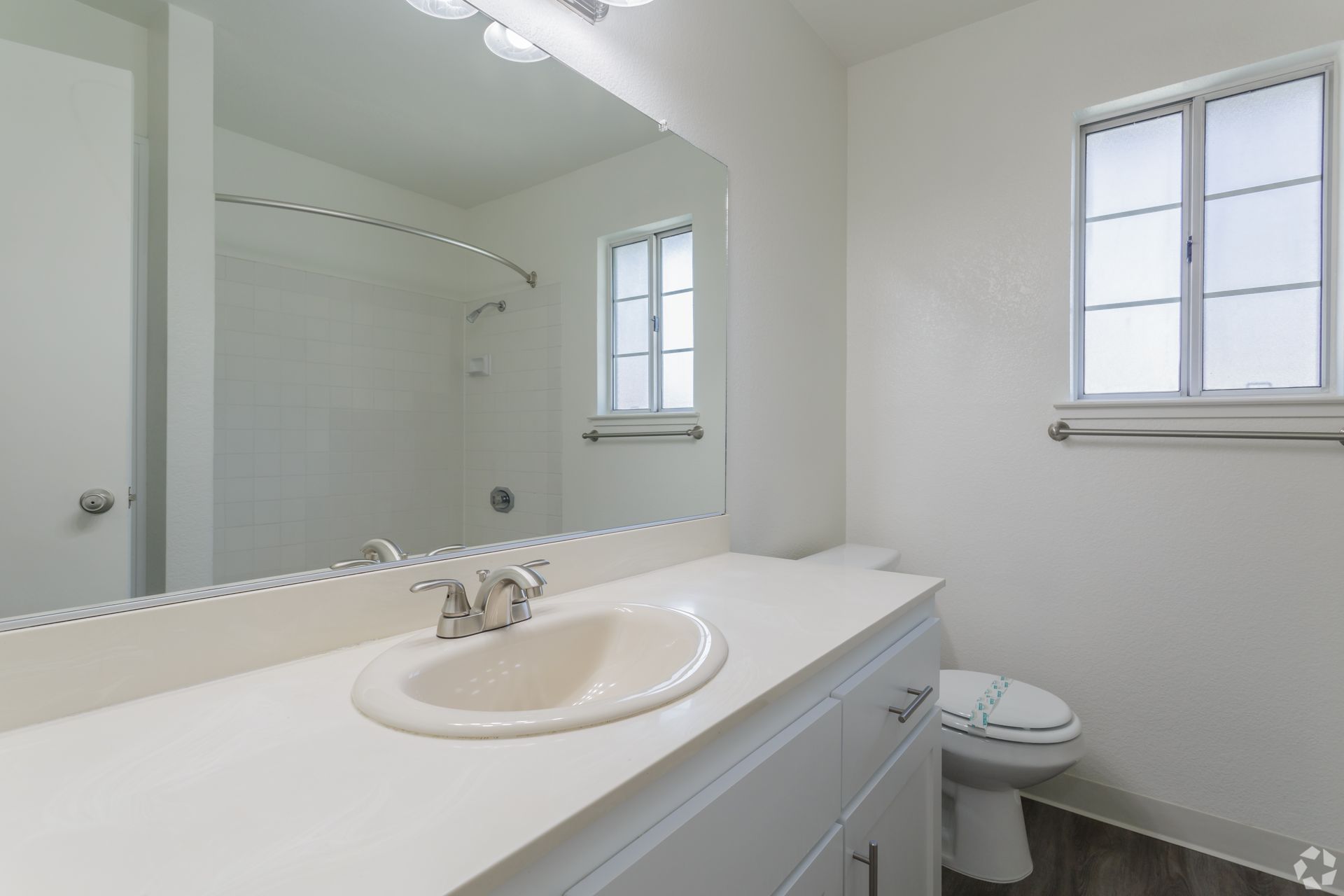 Bathroom with white vanity, sink, toilet, and window. Large mirror reflects shower.