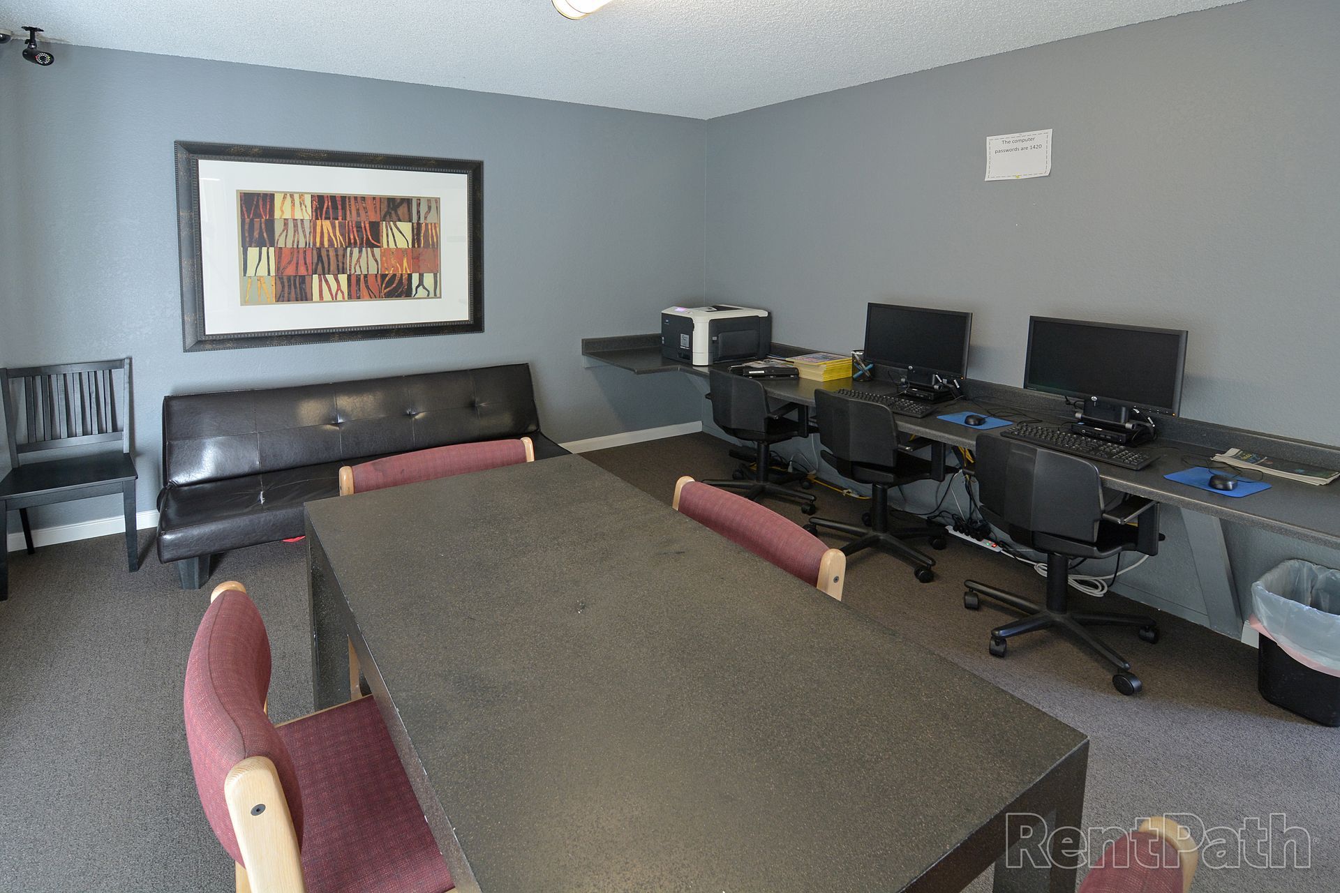 A room with computers, a printer, a table with chairs, and a small couch.