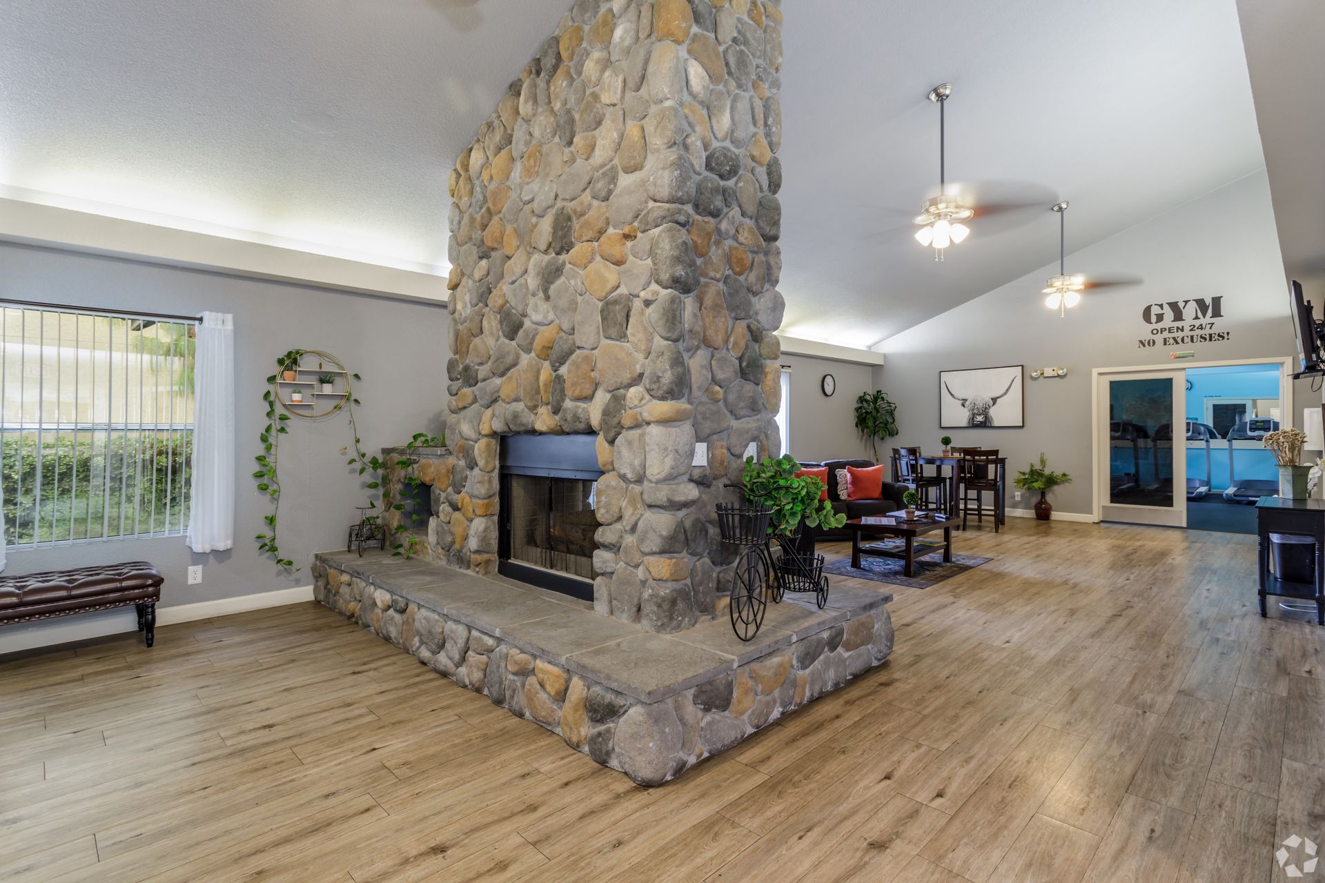 Large stone fireplace in a room with light wood floors, seating area, and a doorway to a gym.