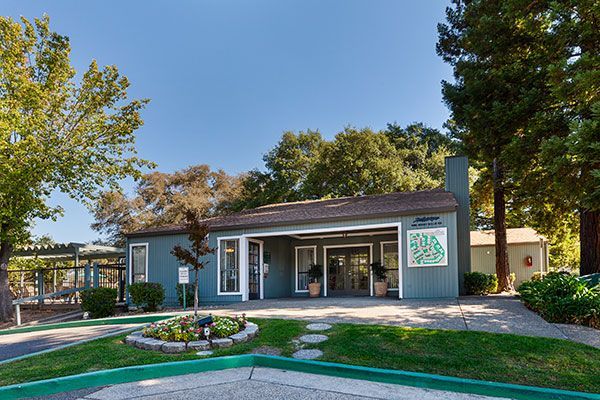 A blue single-story building with a brown roof and a small flower bed in front. Trees surround it.