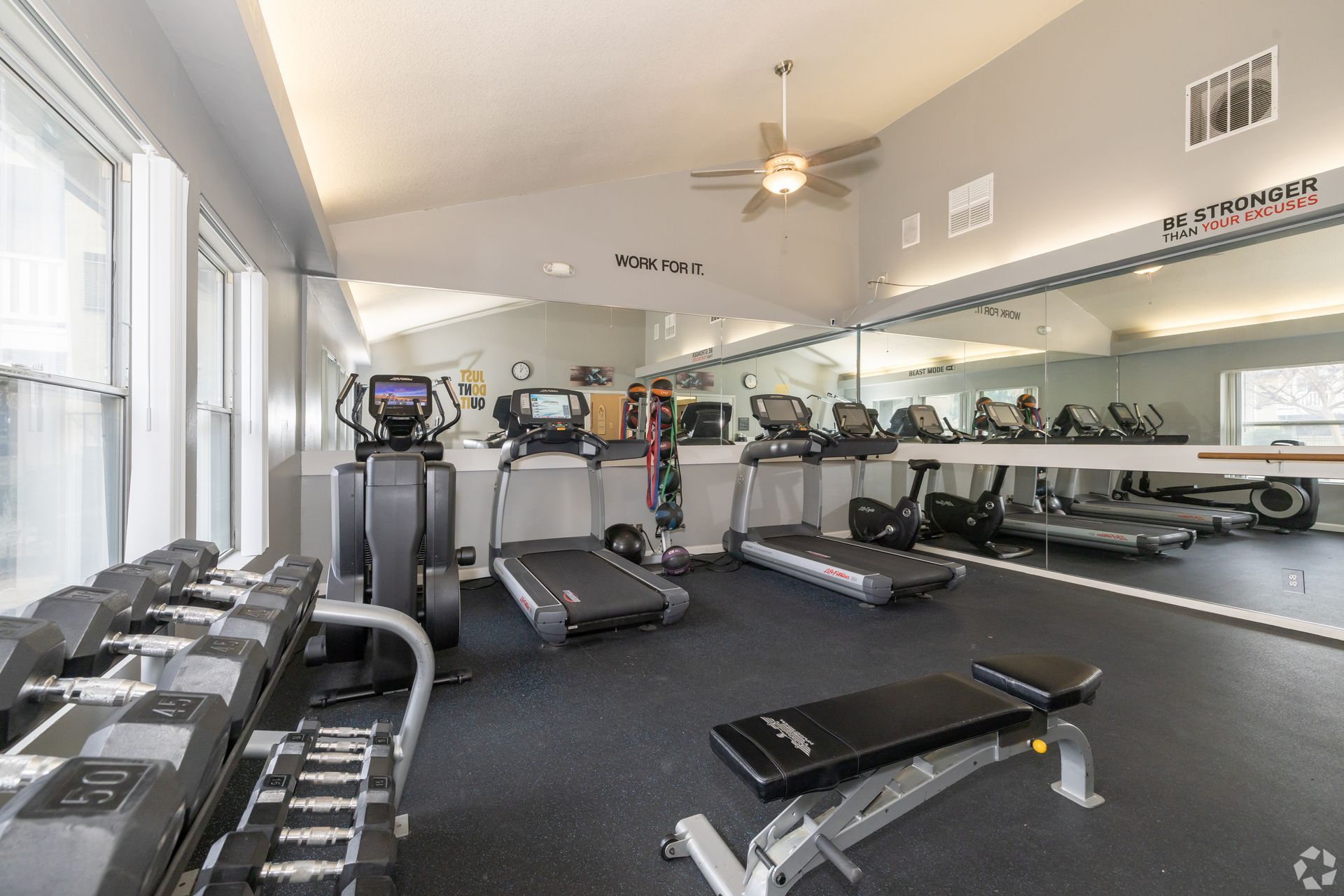 Gym with weight rack, treadmills, elliptical, and exercise bike. Large mirror on wall.