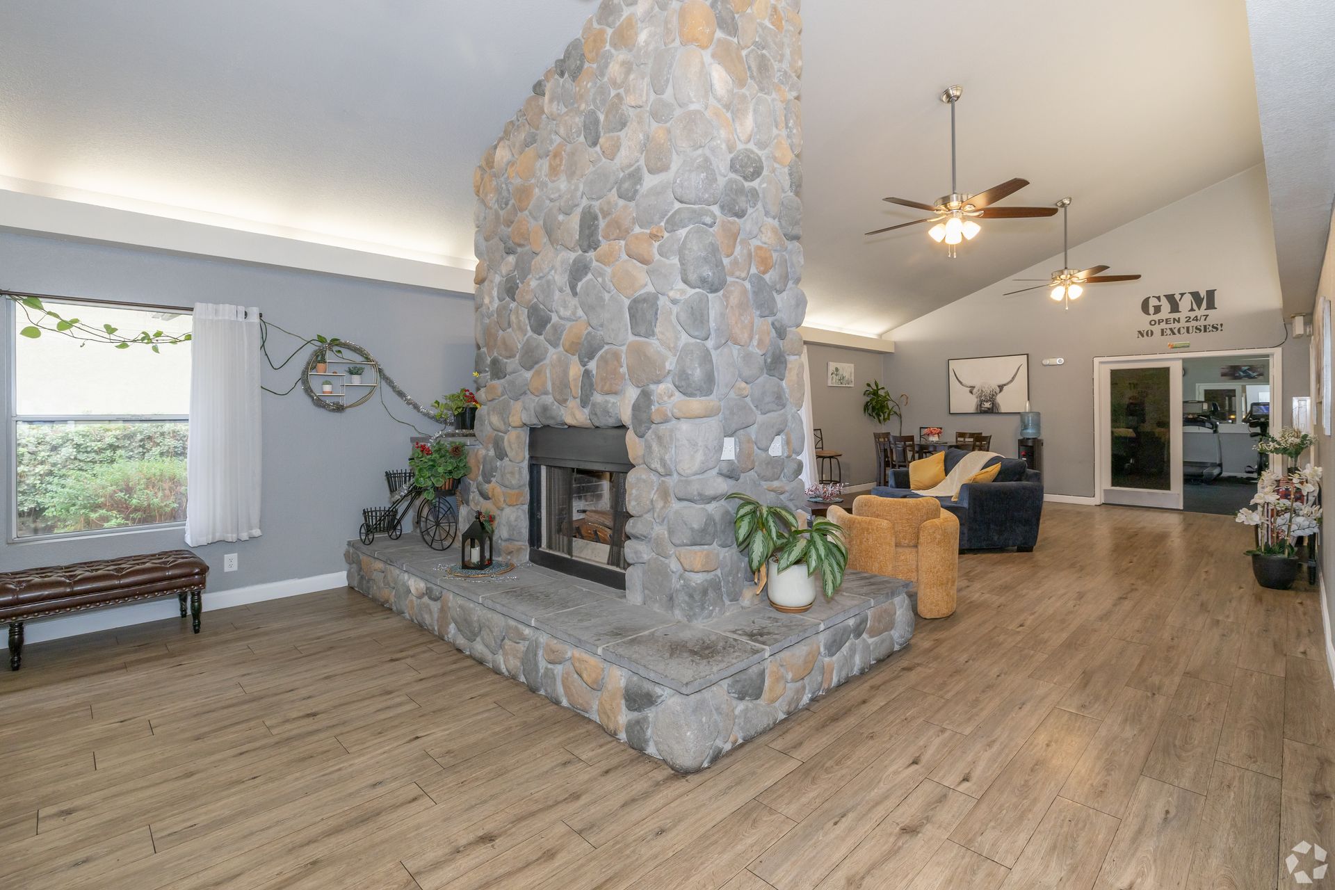 Spacious room with stone fireplace, wooden floor, and a view into a gym.