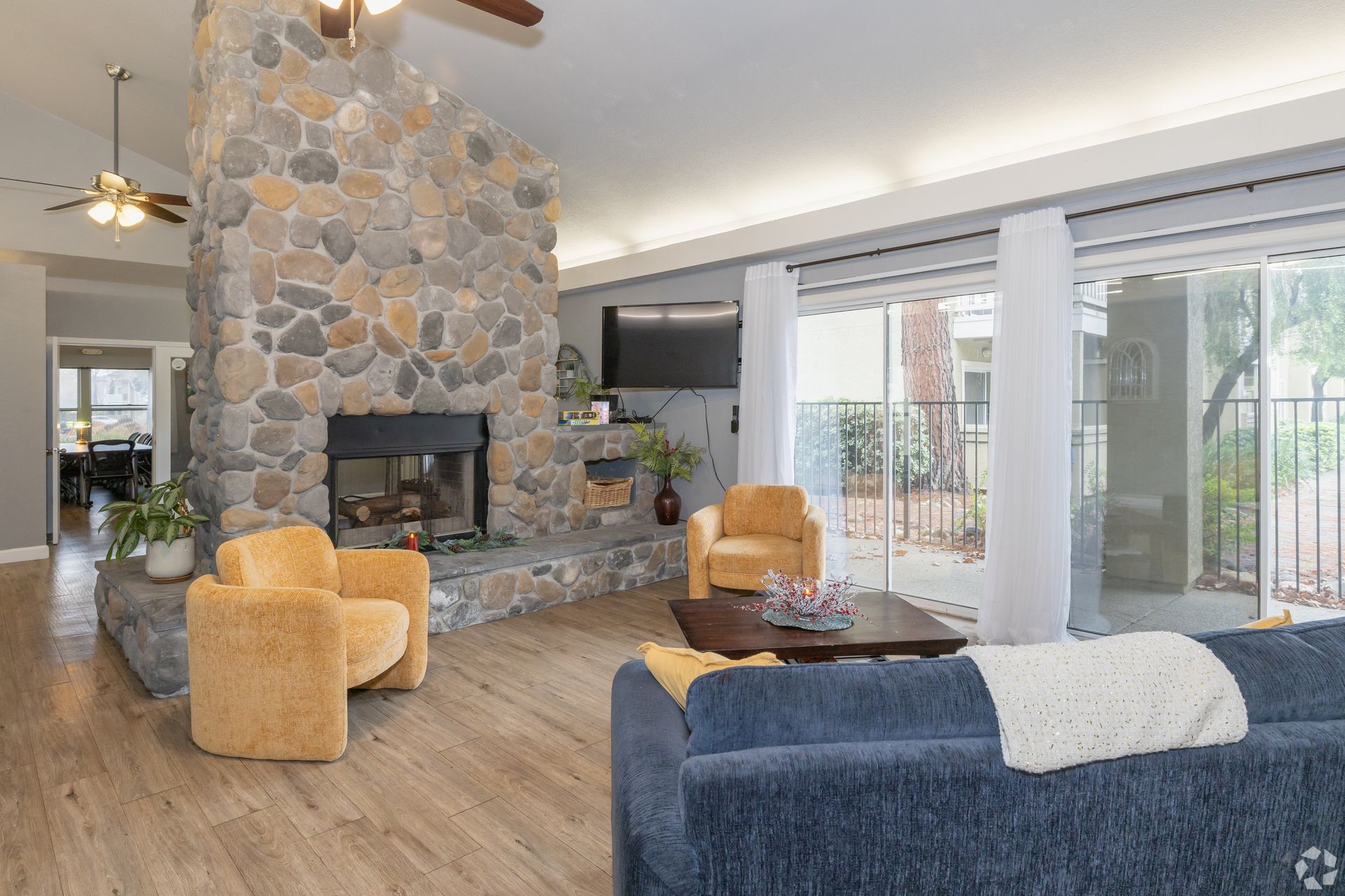 Living room with stone fireplace, yellow armchairs, blue couch, and patio doors.