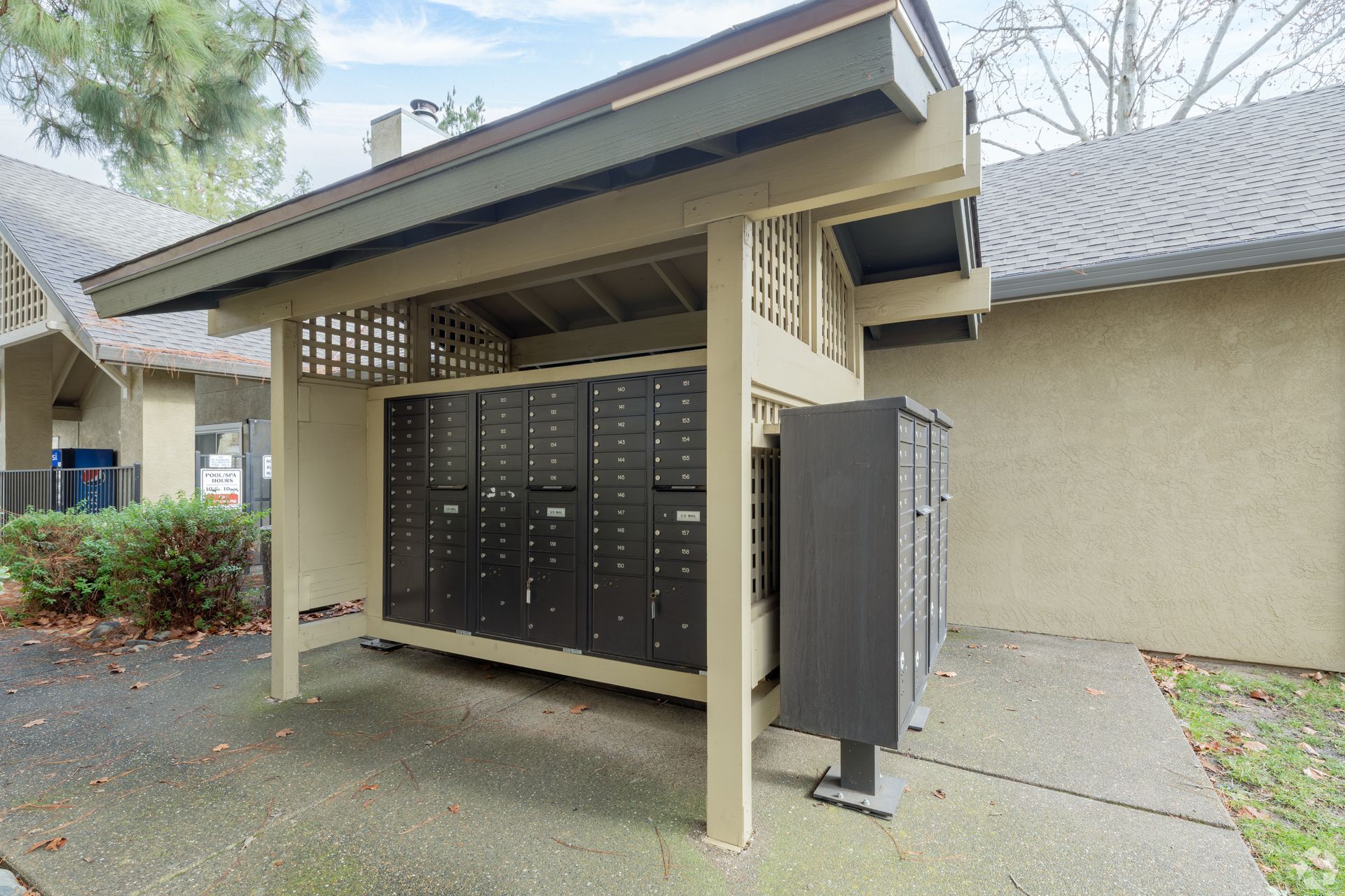 Mailboxes under a covered structure. Black mailboxes, beige wooden frame, concrete path.