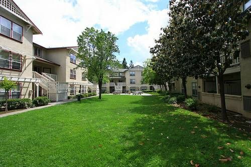 Grassy courtyard with apartment buildings and trees under a partly cloudy sky.