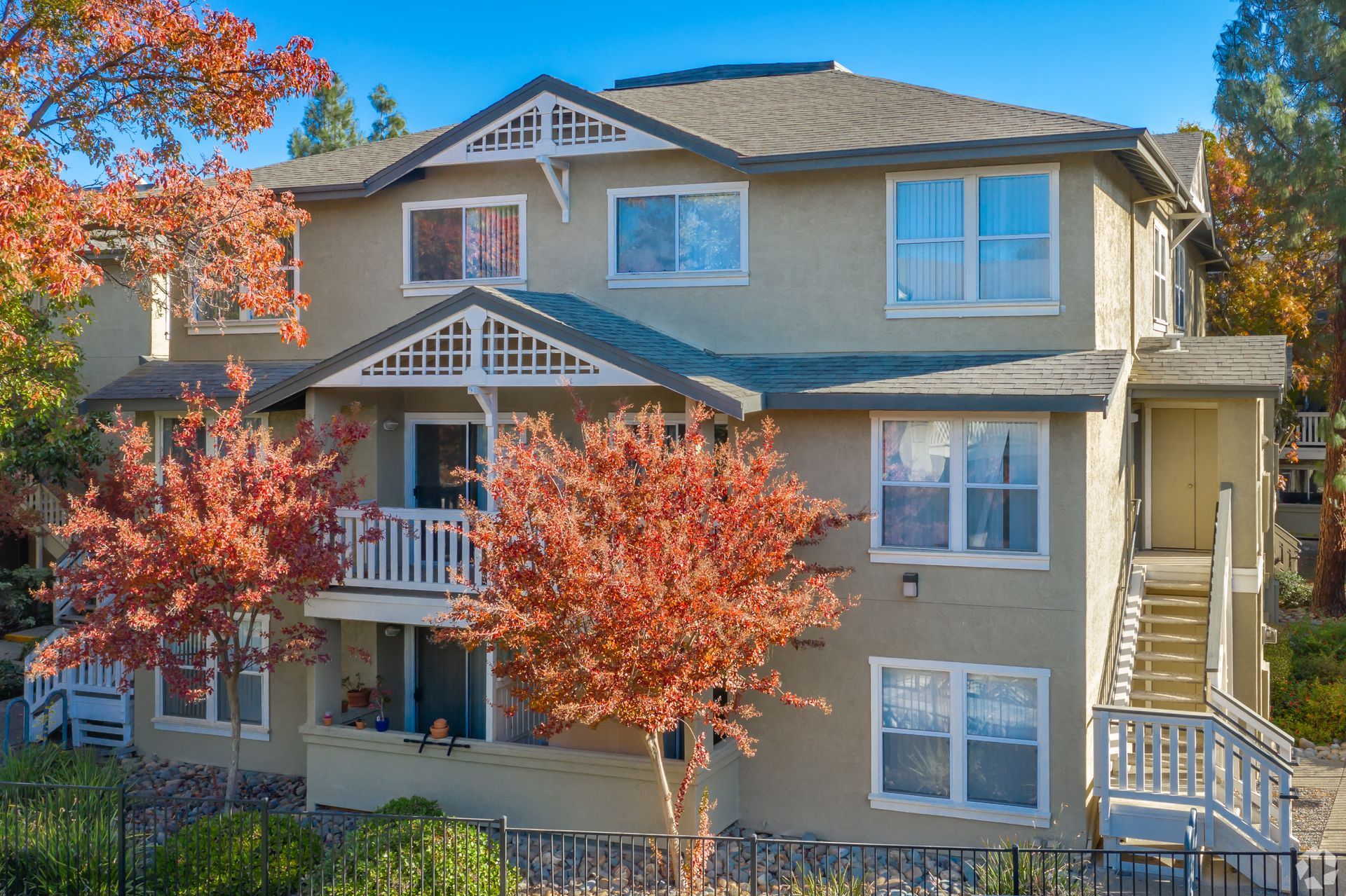 Multi-story beige apartment building with white trim and balconies; red autumn trees.