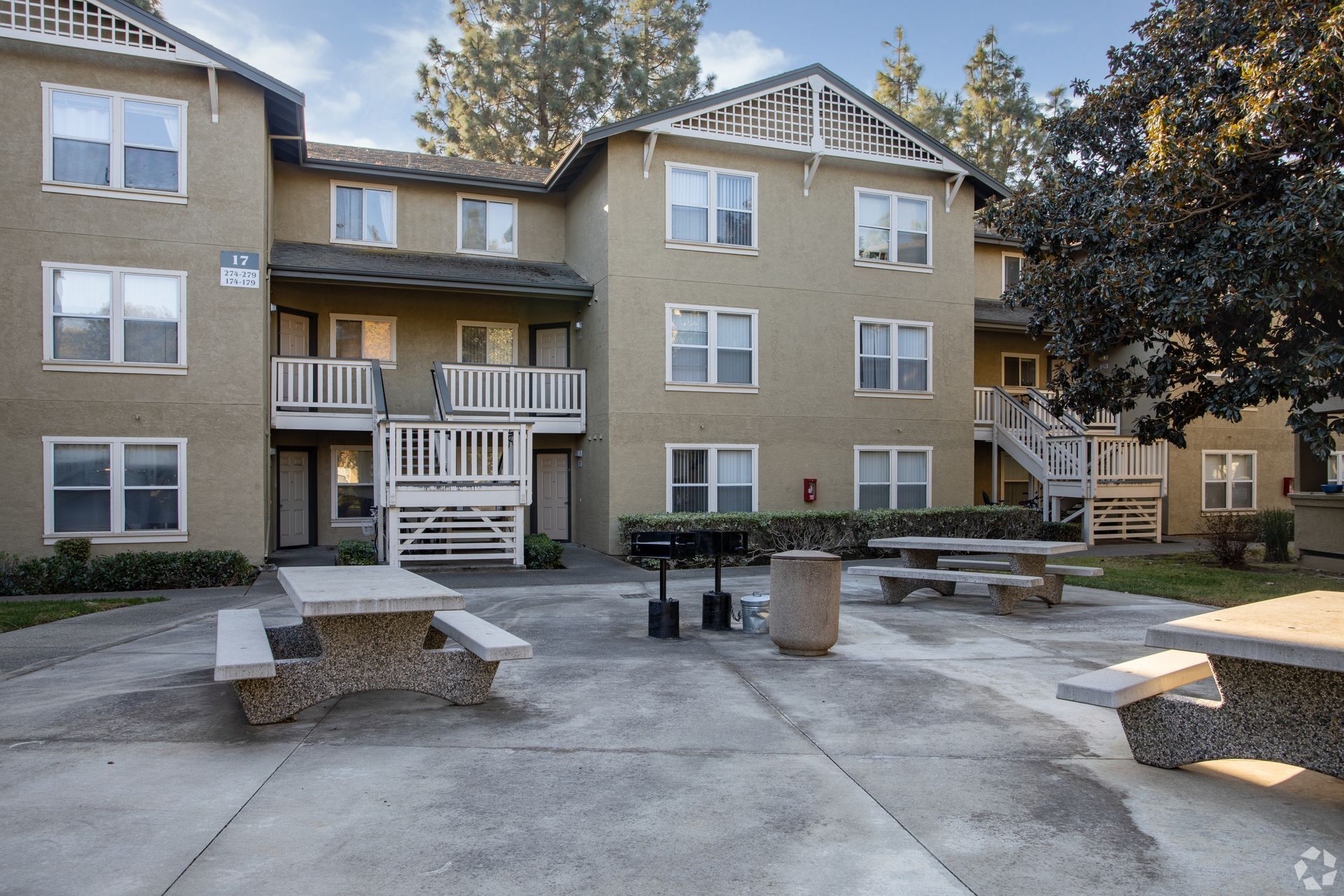 Apartment building exterior with picnic tables, grill, and concrete patio.