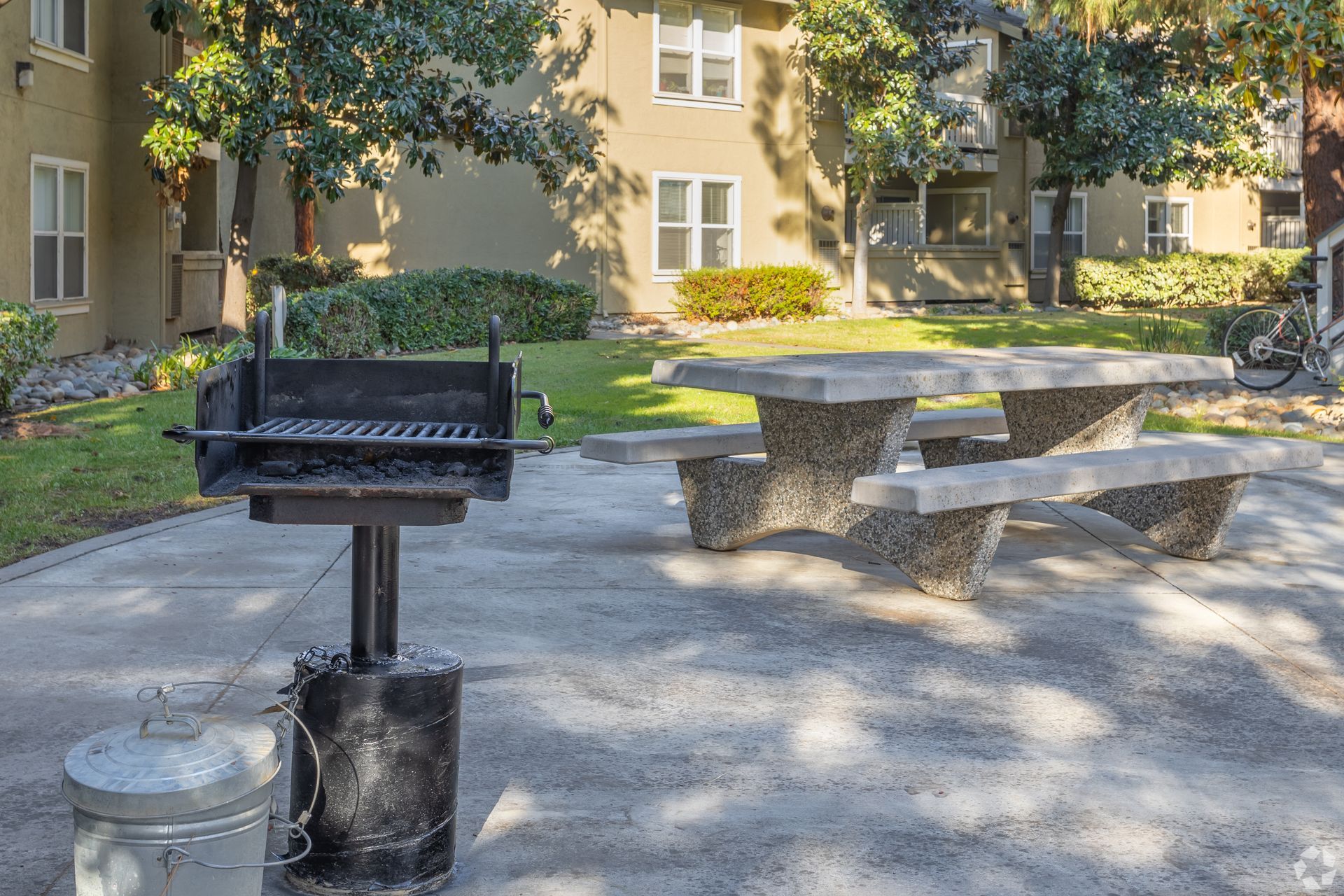 Grill and concrete picnic table on patio in front of apartment building.