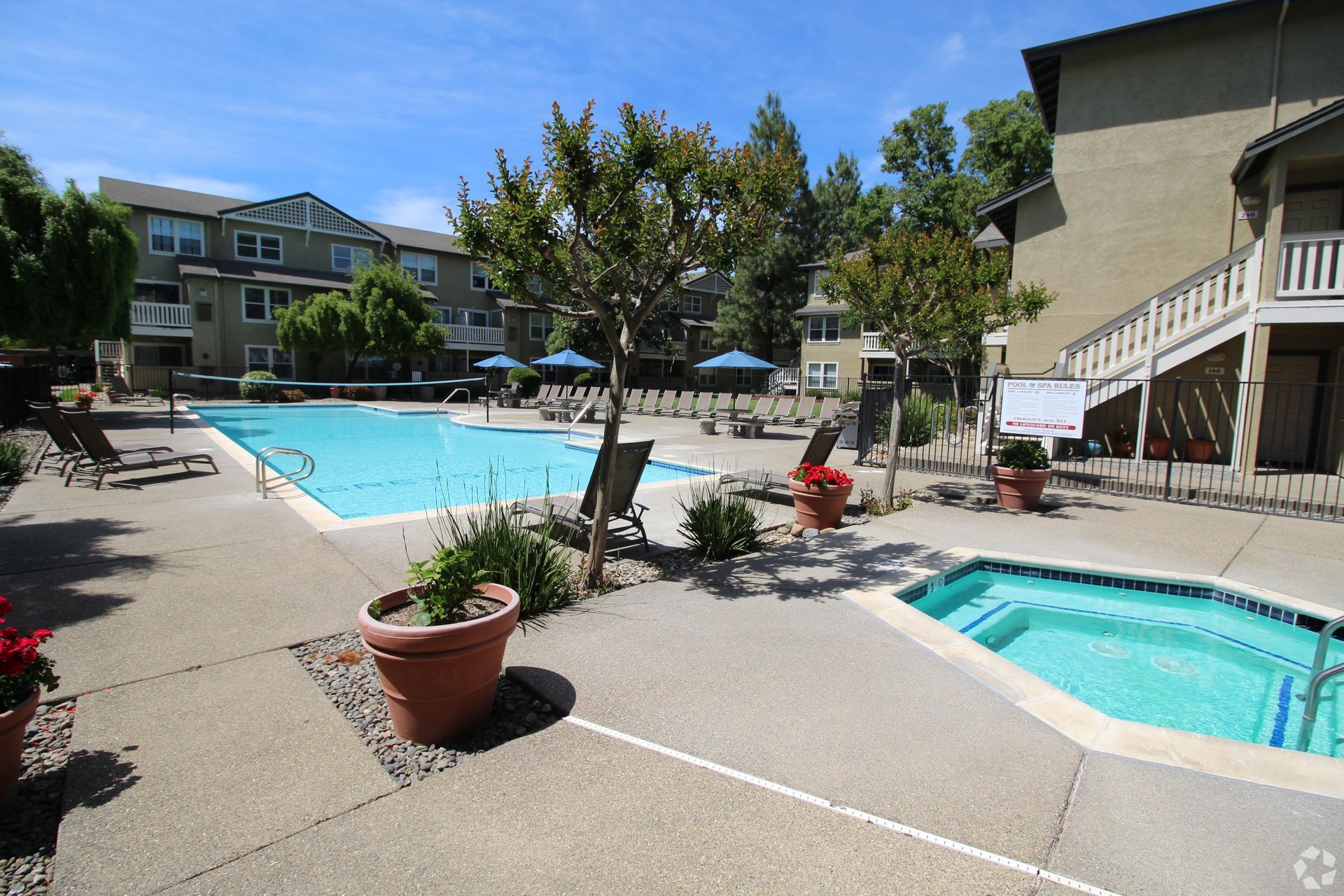 Pool and jacuzzi in apartment complex courtyard, blue water, sunny day.