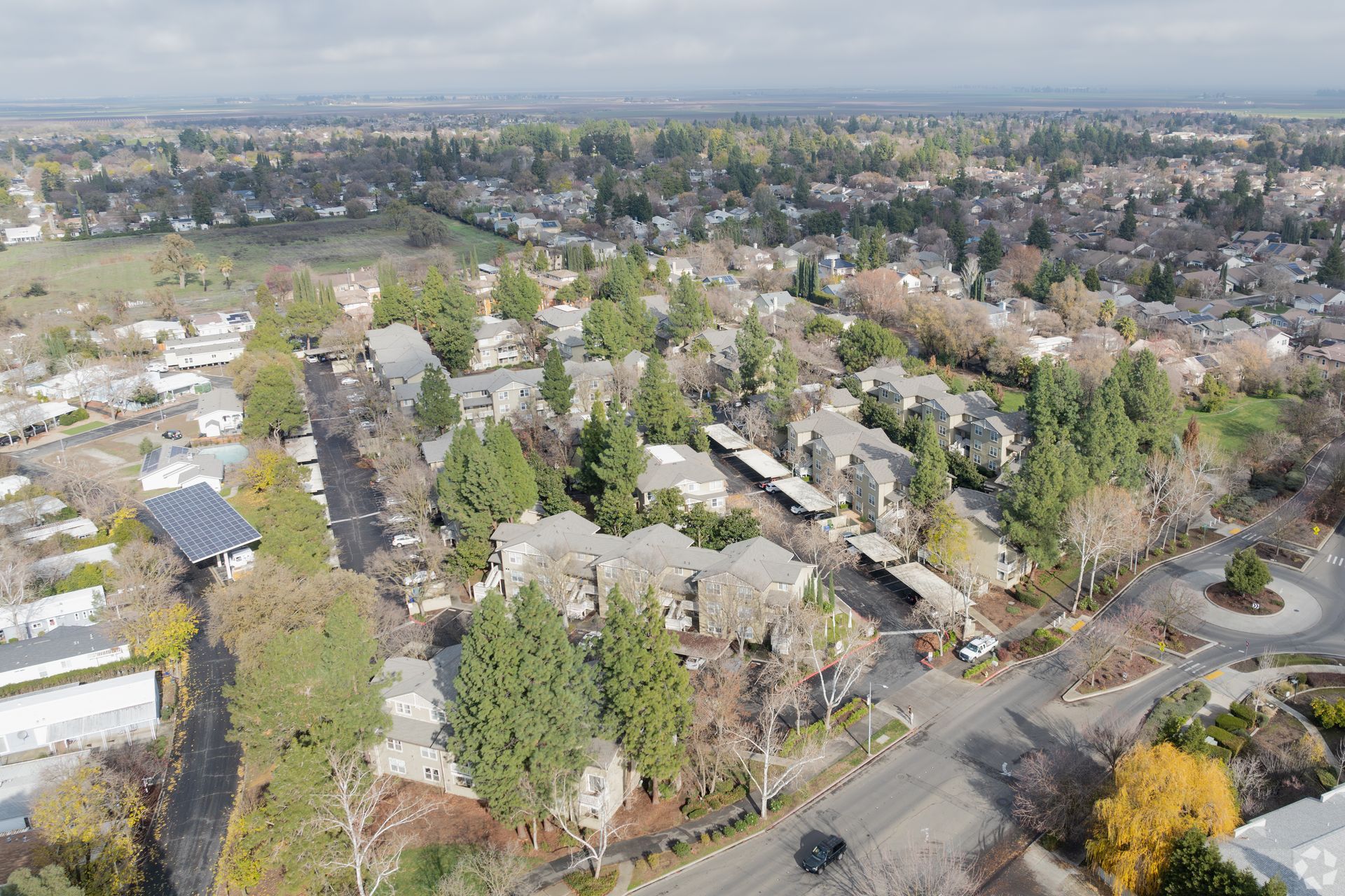 Aerial view of suburban neighborhood with houses, streets, and trees on a cloudy day.