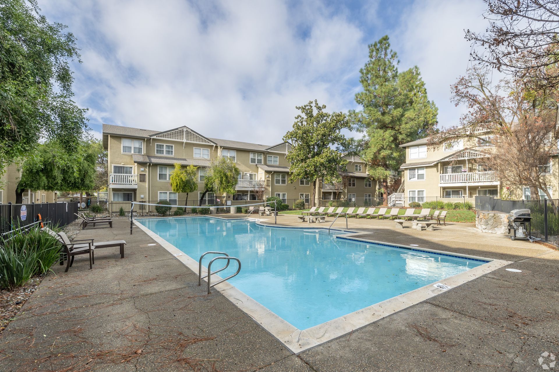 Swimming pool in front of an apartment complex, surrounded by trees. Cloudy sky.