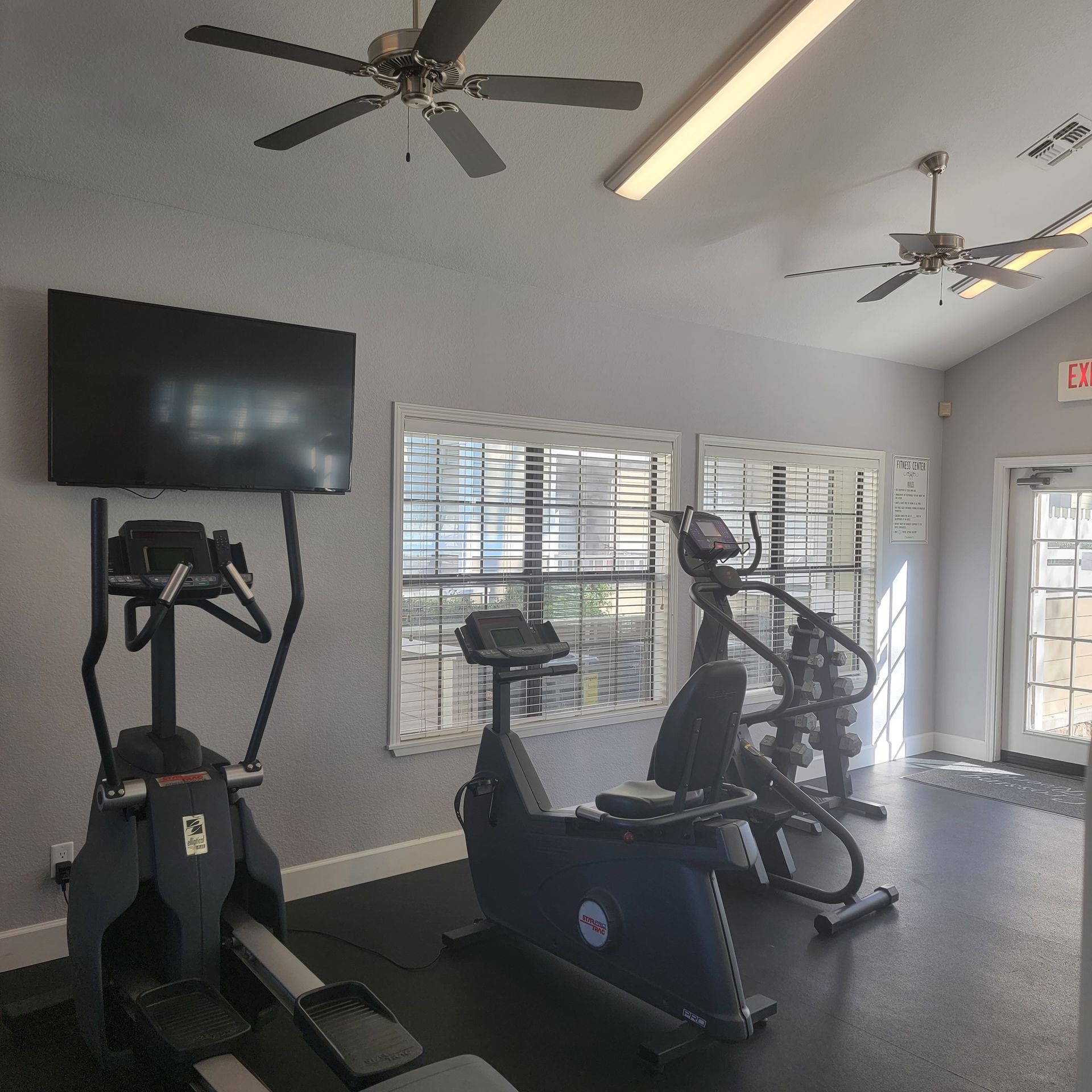 Gym with exercise equipment, including a rowing machine, stationary bike, and elliptical machine. TV on the wall.