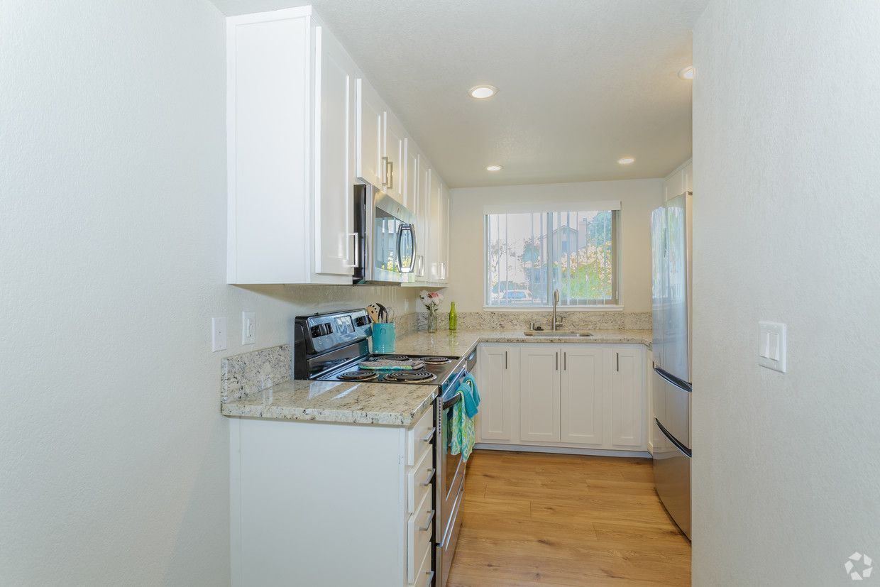 White kitchen with light wood flooring, granite countertops, and stainless steel appliances.
