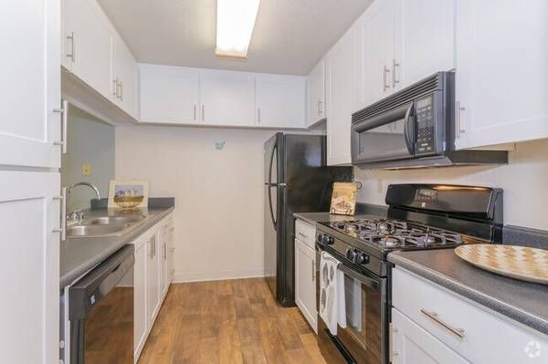 Small, galley-style kitchen with white cabinets, black appliances, and wooden floors.