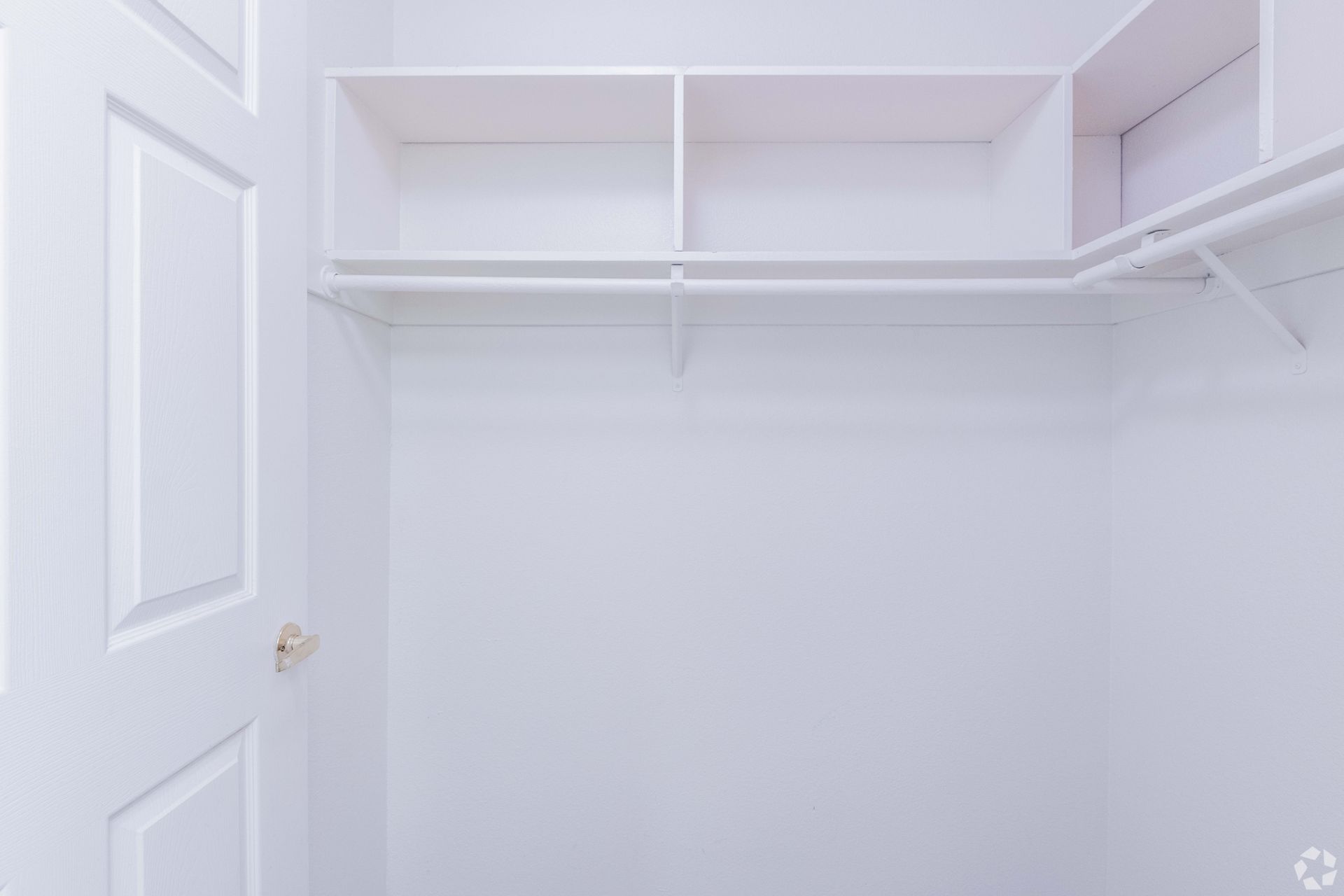White, empty closet with built-in shelves and a clothes rod. A white door is partially open.