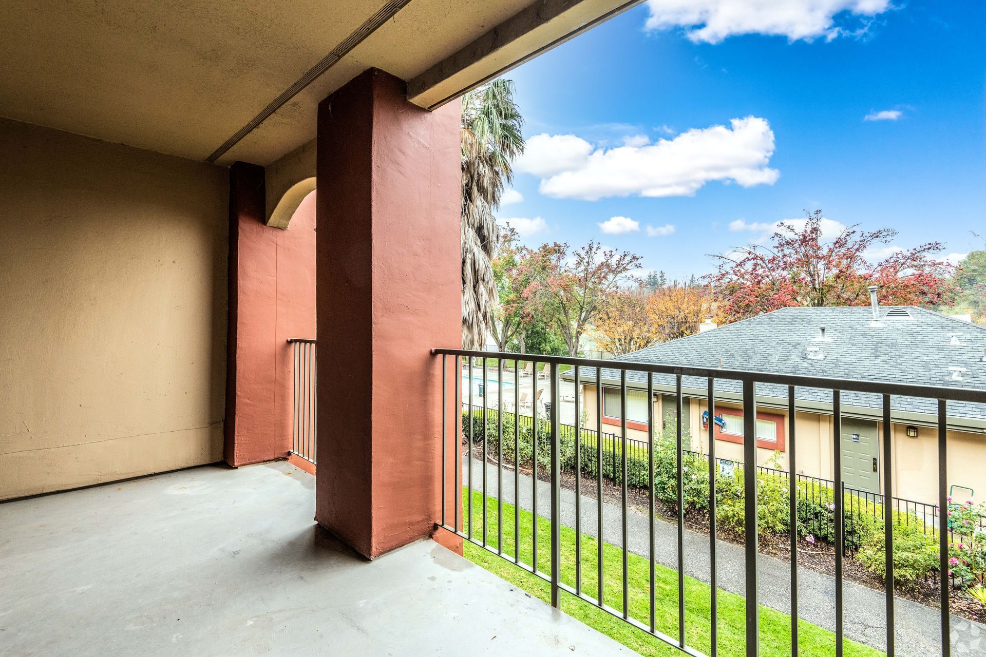 Balcony overlooking neighborhood with blue sky, trees, and green grass.