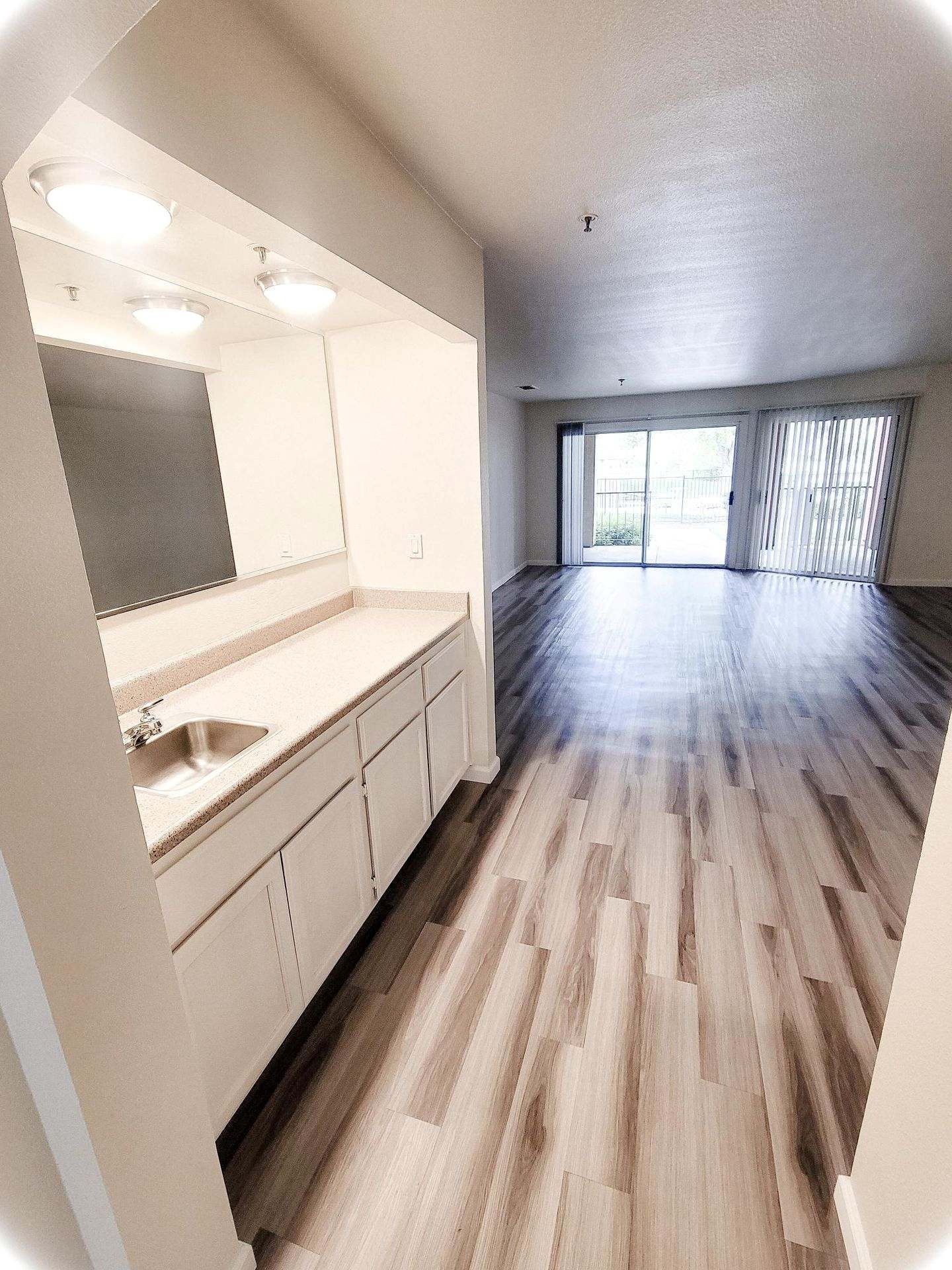 Interior view of an apartment with a wet bar, wood floors, and sliding glass doors leading to a patio.