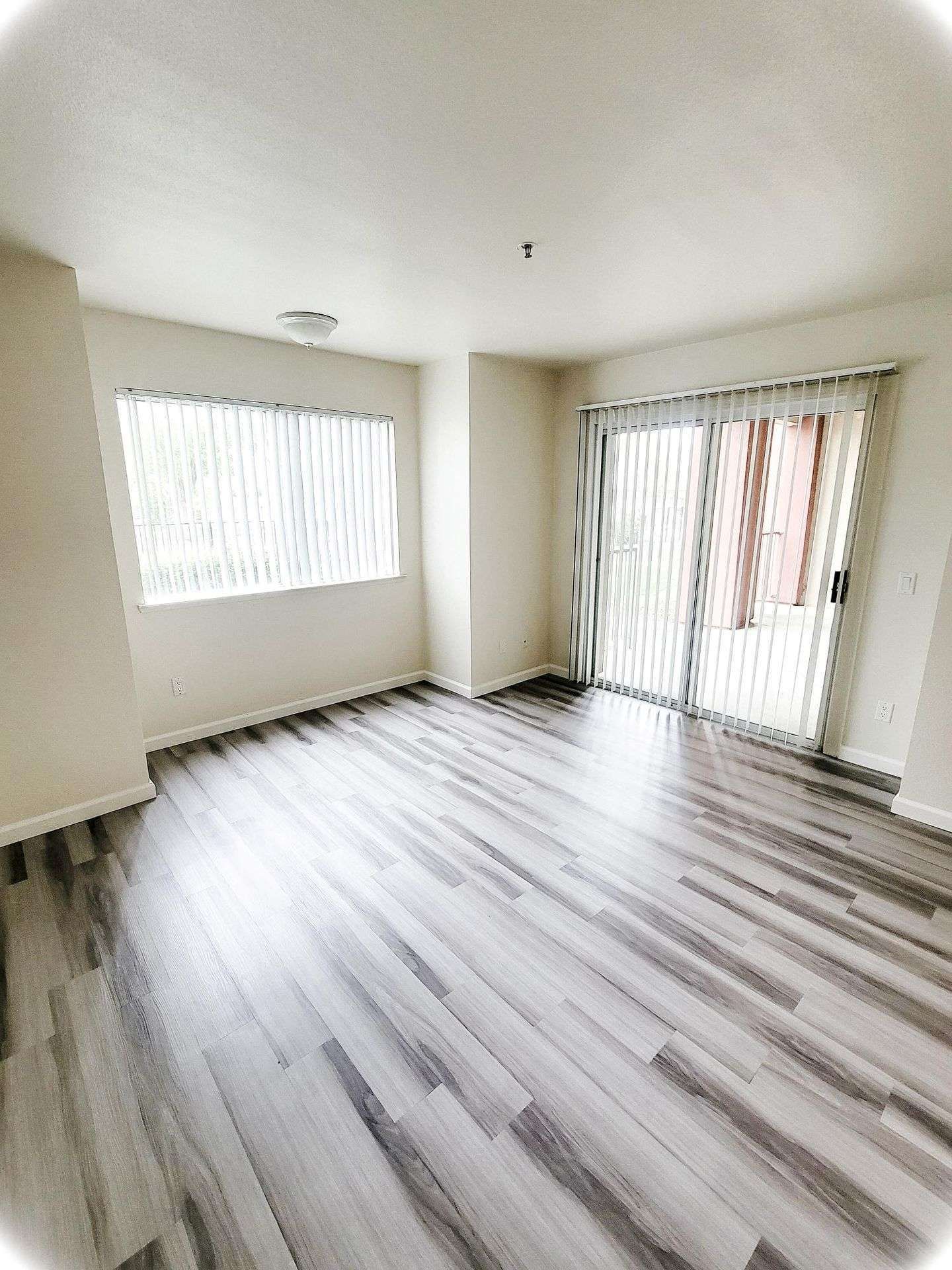 Empty room with wood-look flooring, large window with blinds, and sliding glass door.