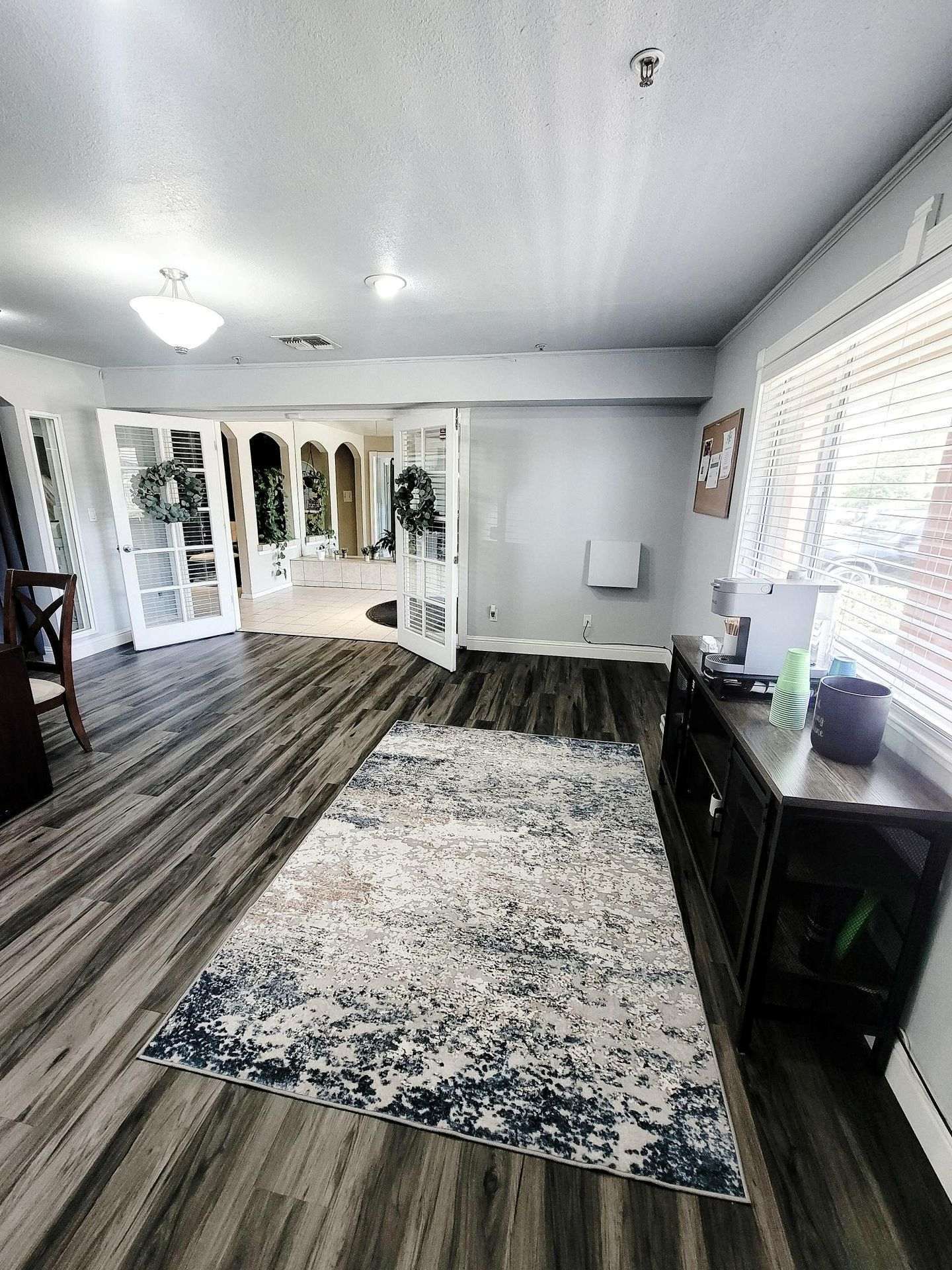 Spacious room with dark wood flooring, a rug, and glass doors leading to another area.