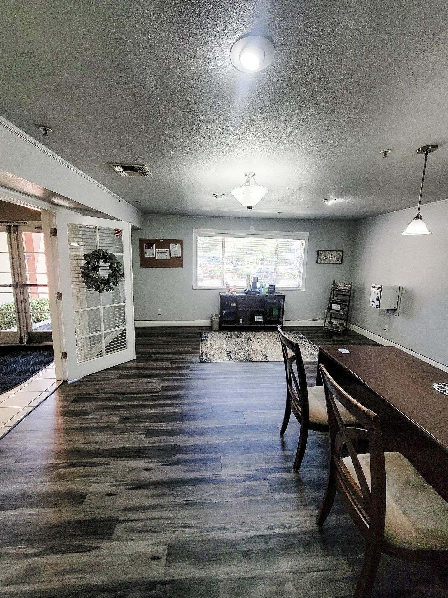 Spacious room with dark wood flooring, light gray walls, and French doors. There's a table with chairs and a TV area.