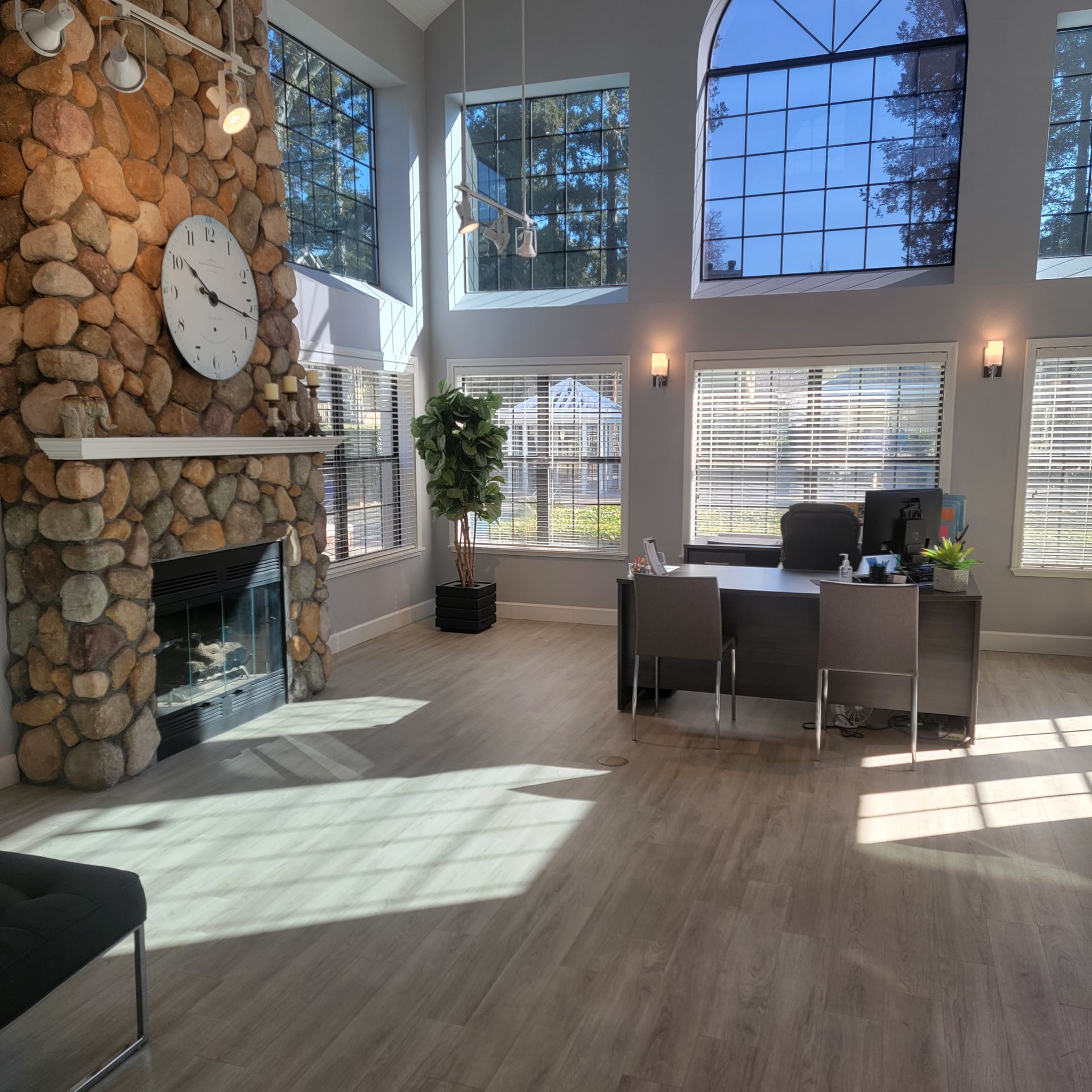 Lobby with stone fireplace, large windows, desk, and clock. Sunlight streams through.