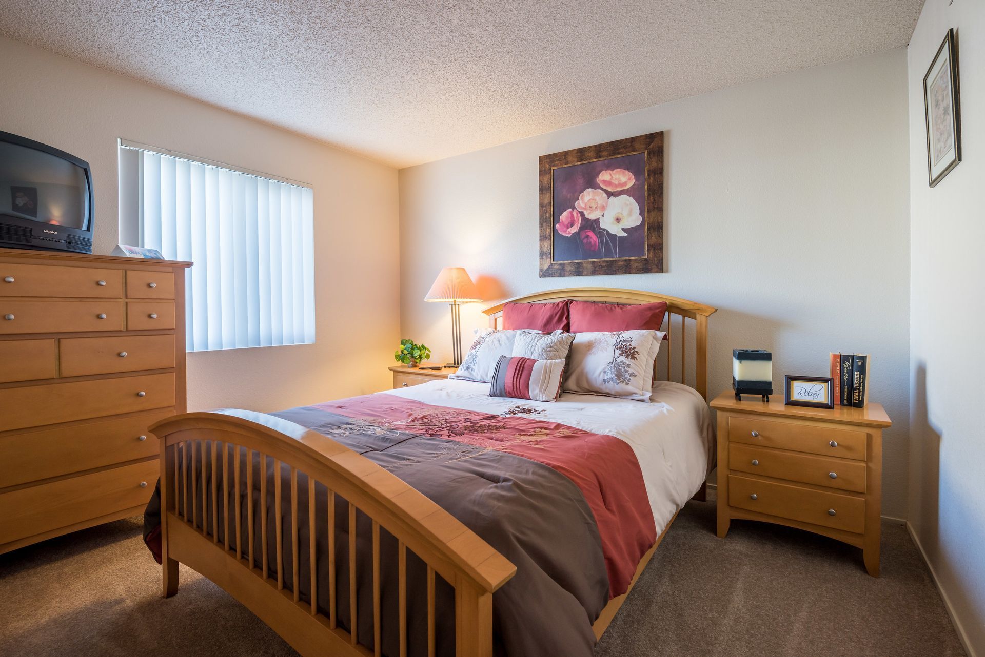 Bedroom with light brown furniture, bed with decorative pillows, window, and TV.