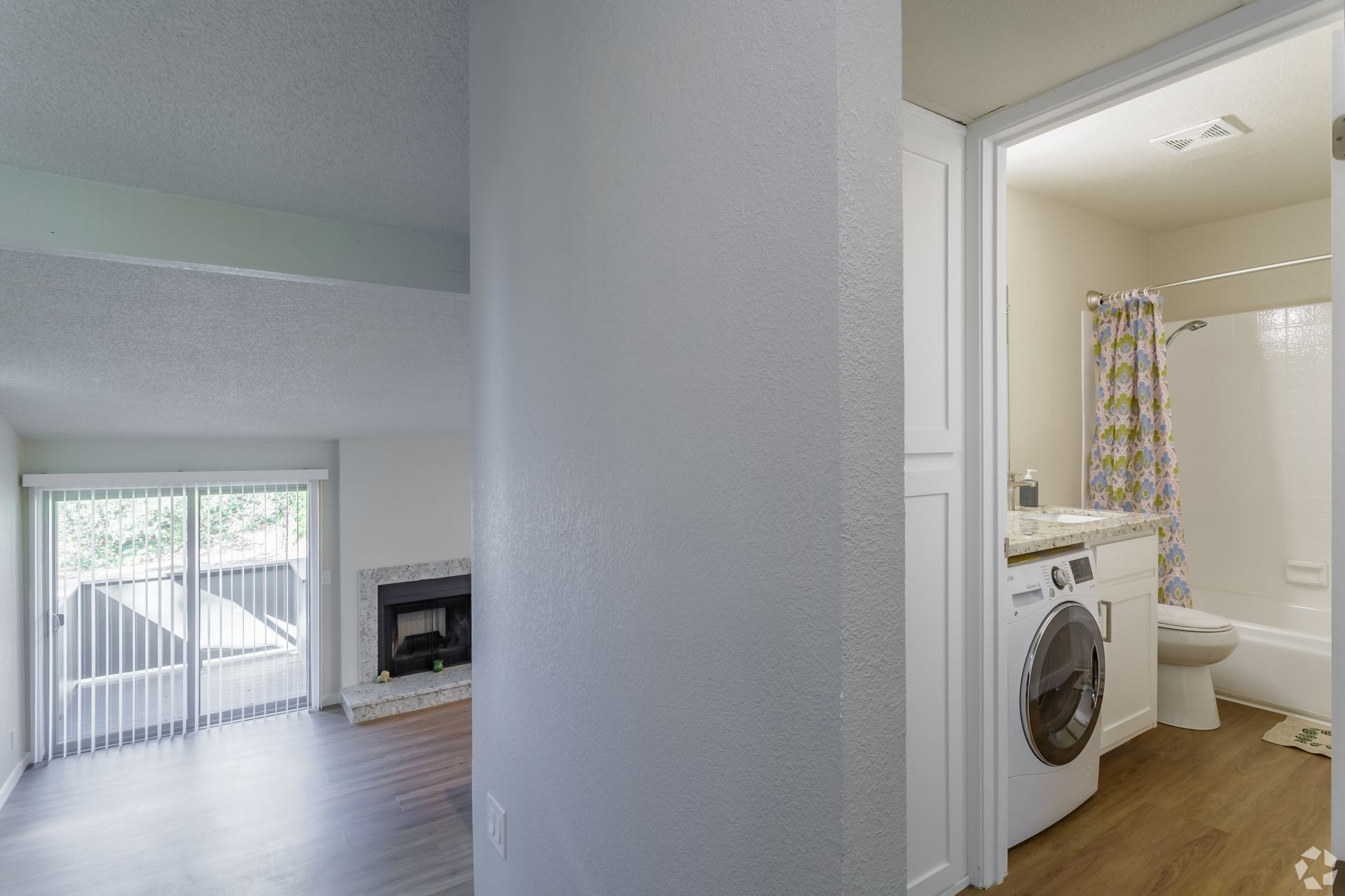 Interior view of a living space with a fireplace and sliding door, and a bathroom with a washing machine.