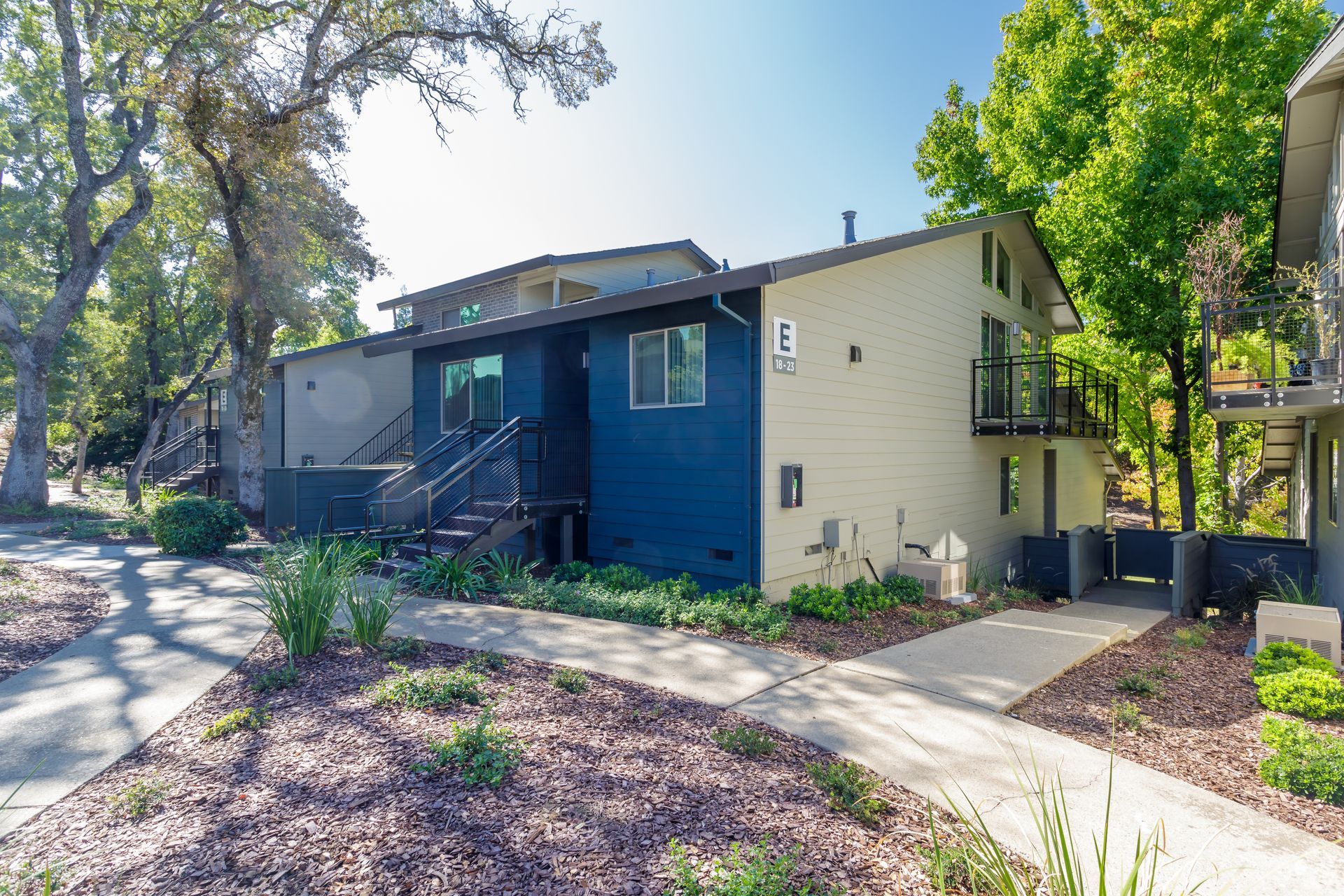 Building with blue and beige siding, a walkway, and surrounding trees.