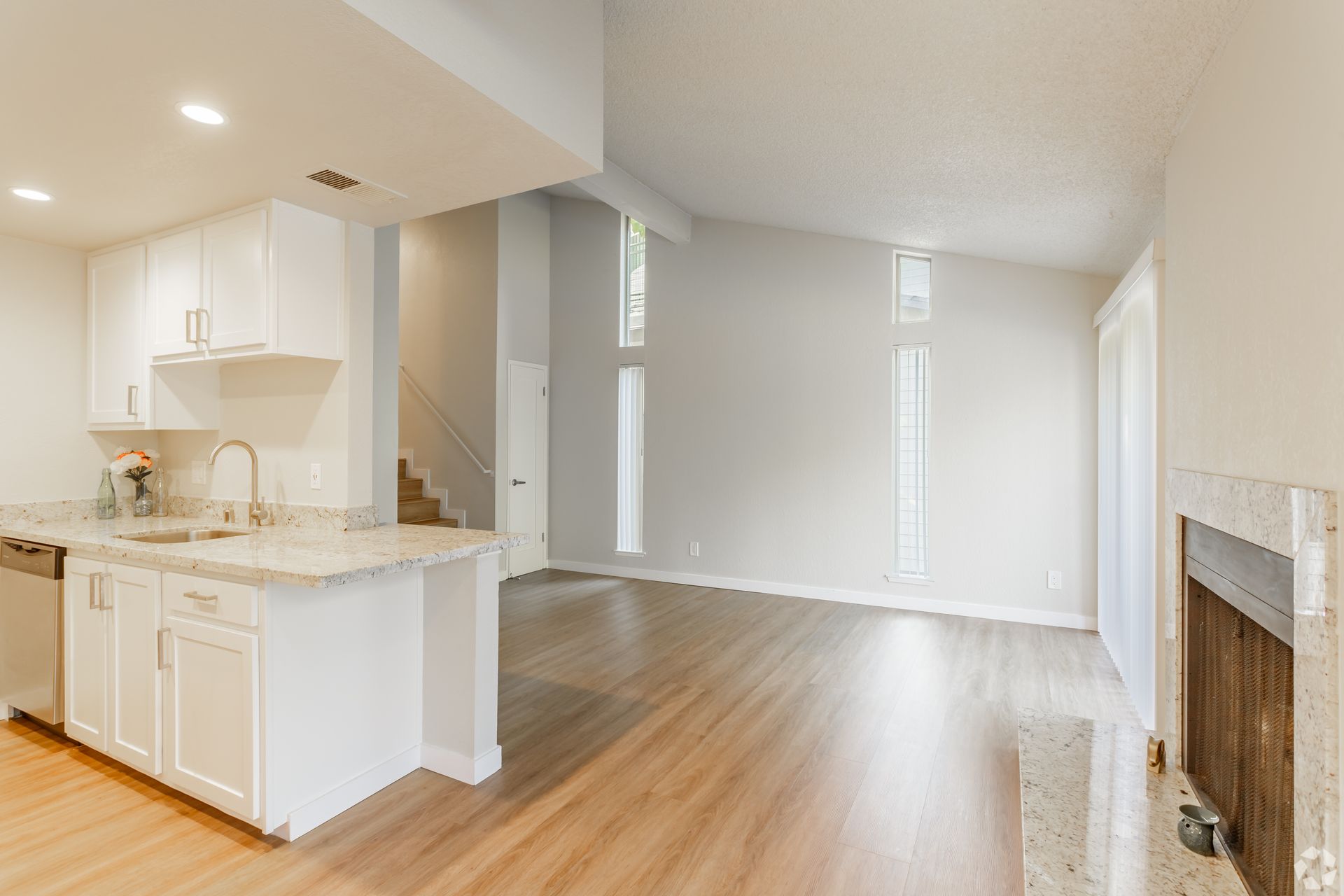 Kitchen and living room with white cabinets, light wood floors, and tall windows.