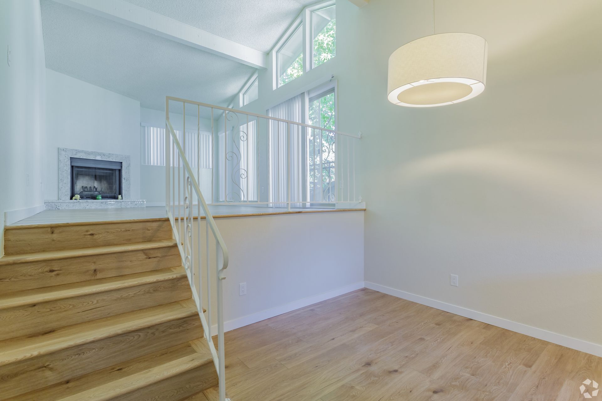 Staircase with light wood steps leading to a raised area with fireplace and large windows.