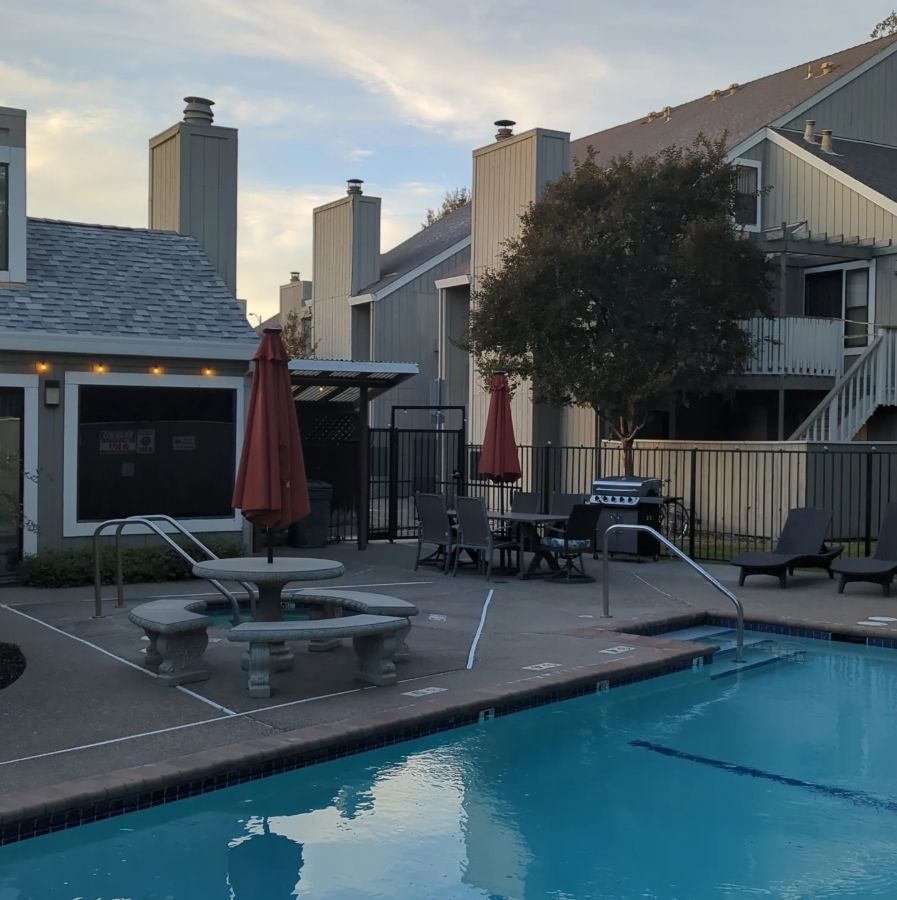 Pool area with umbrellas, tables, and chairs near apartment buildings.
