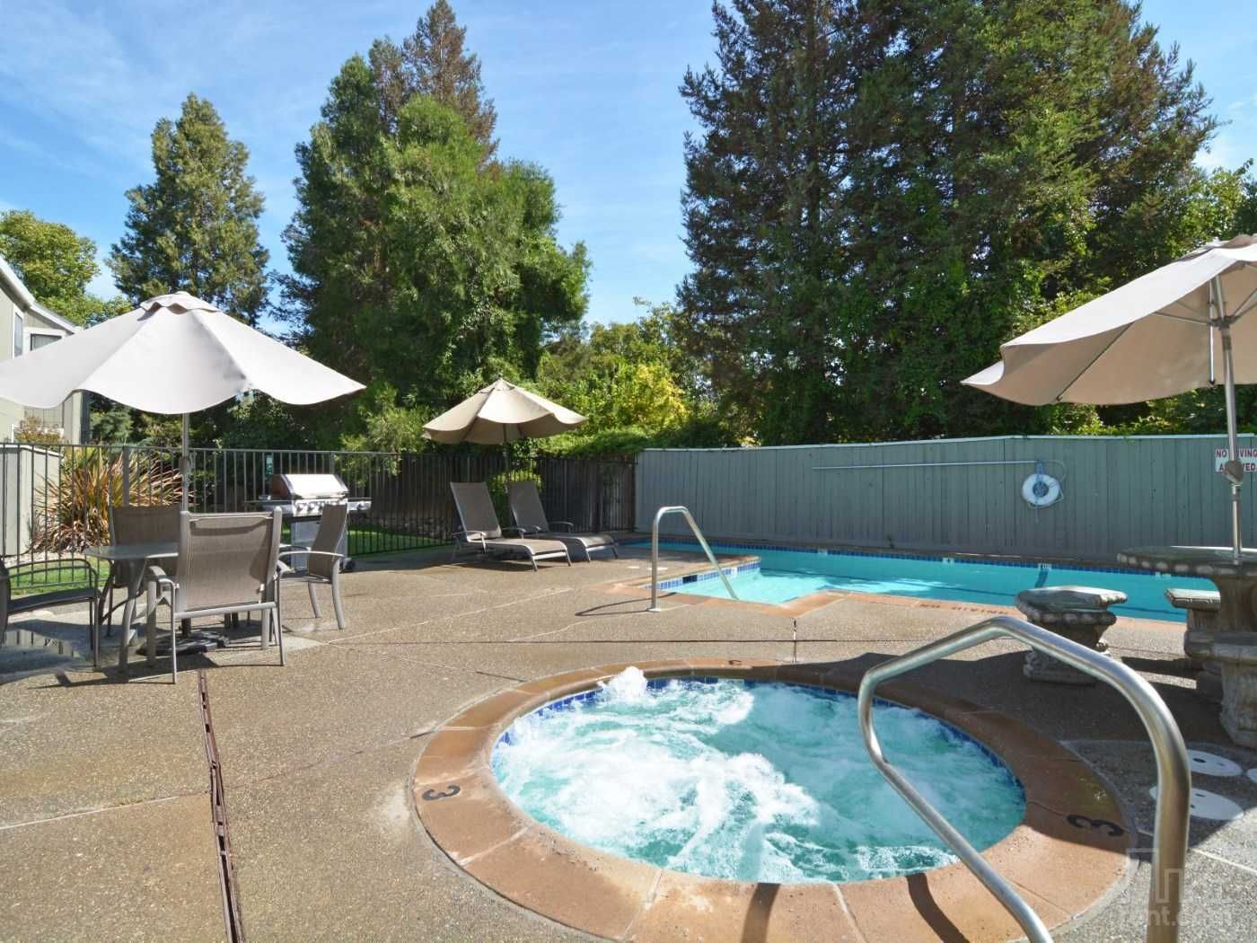 A backyard with a hot tub and pool, lounge chairs, a grill, and umbrellas.