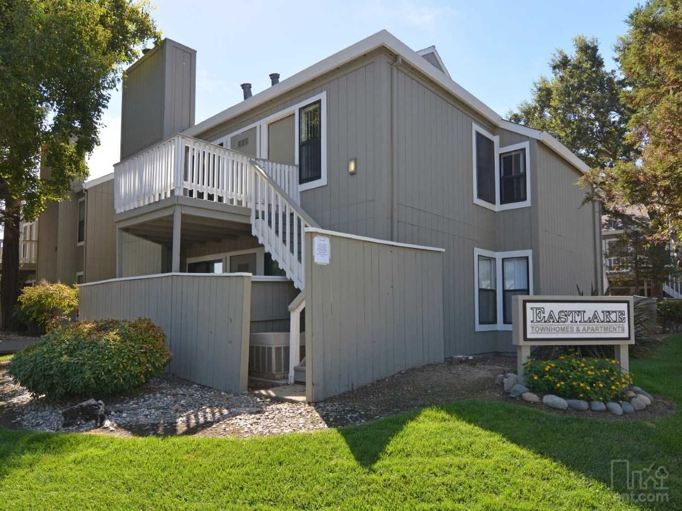 Gray two-story apartment building with white stairs and balcony, sign reads 