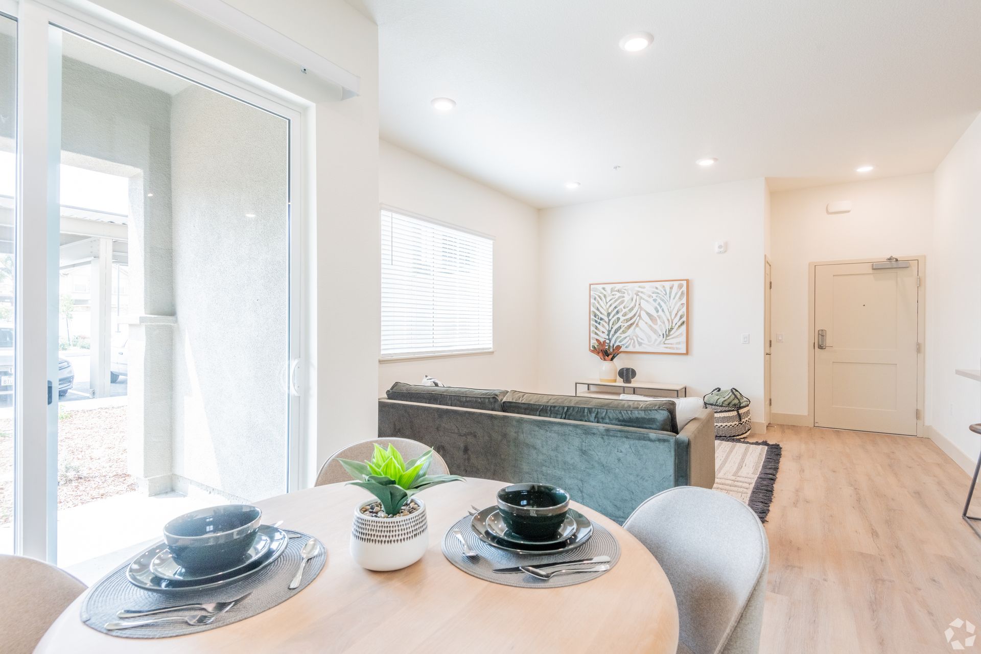 Dining area with round table set for two, and a living area with a sofa. Bright, neutral colors.