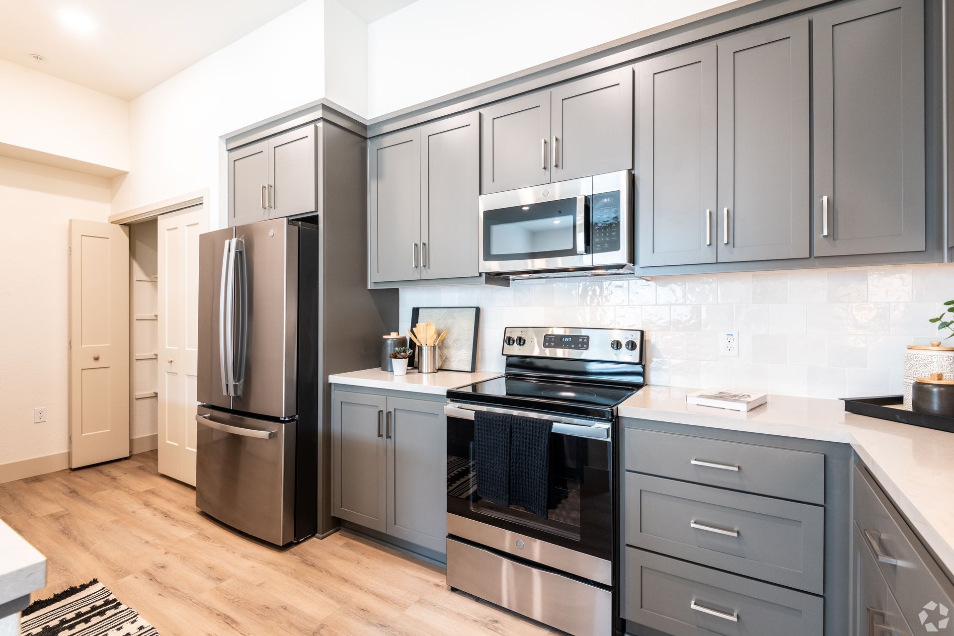 Modern kitchen with gray cabinets, stainless steel appliances, and white countertops.