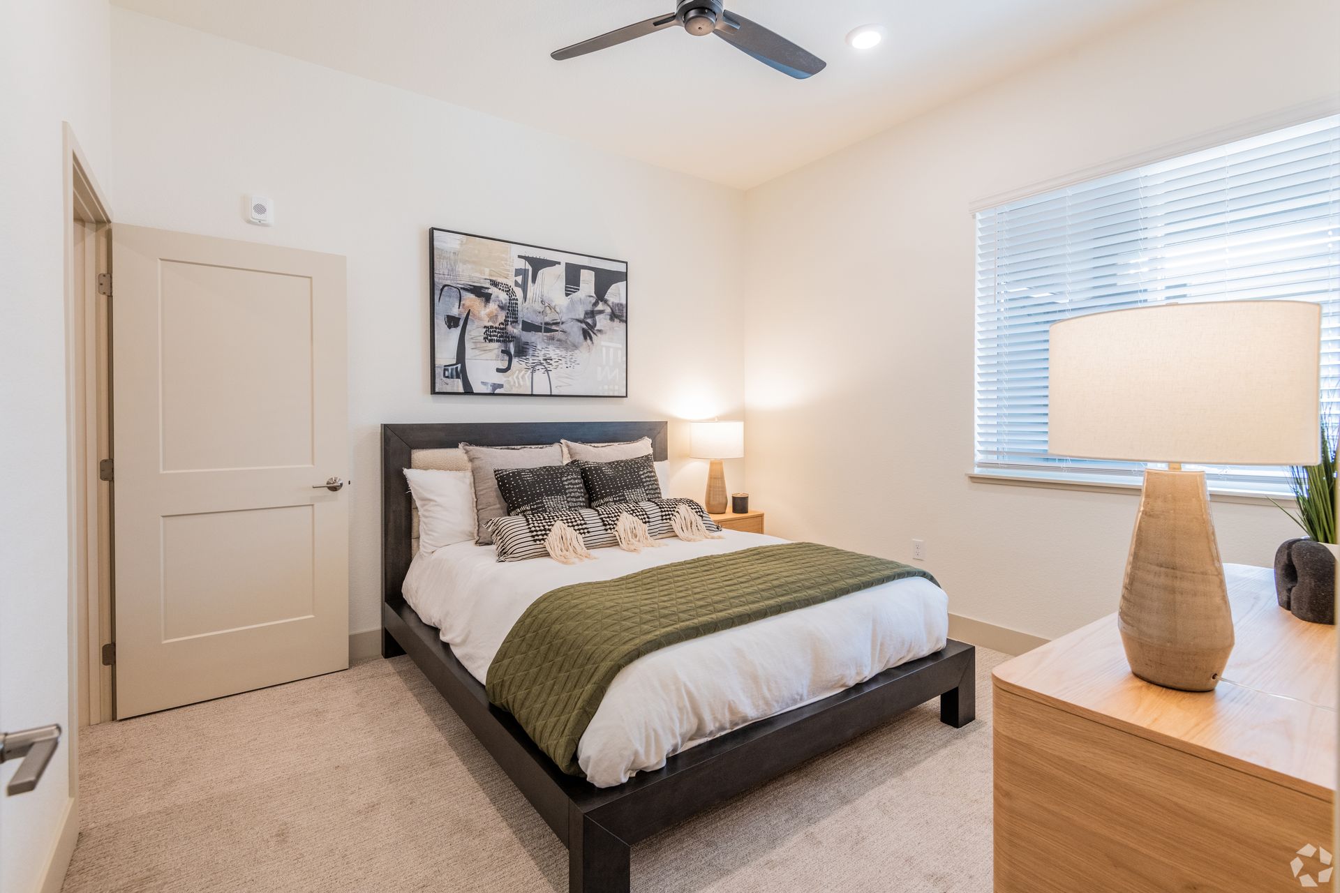Bedroom with bed, nightstand, art, window, and door; neutral colors.