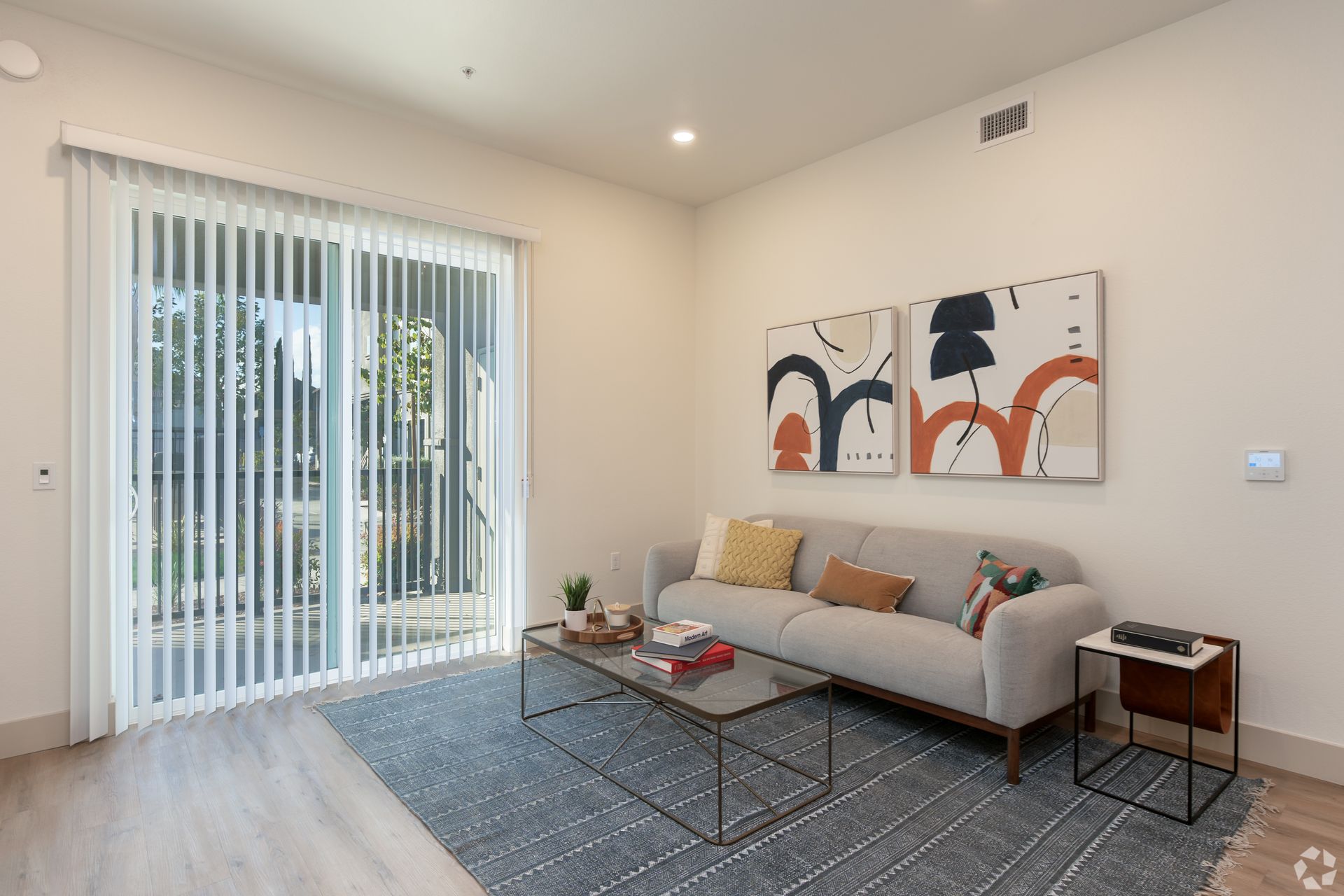 Modern living room with sliding glass door, grey couch, abstract art, and blue rug.