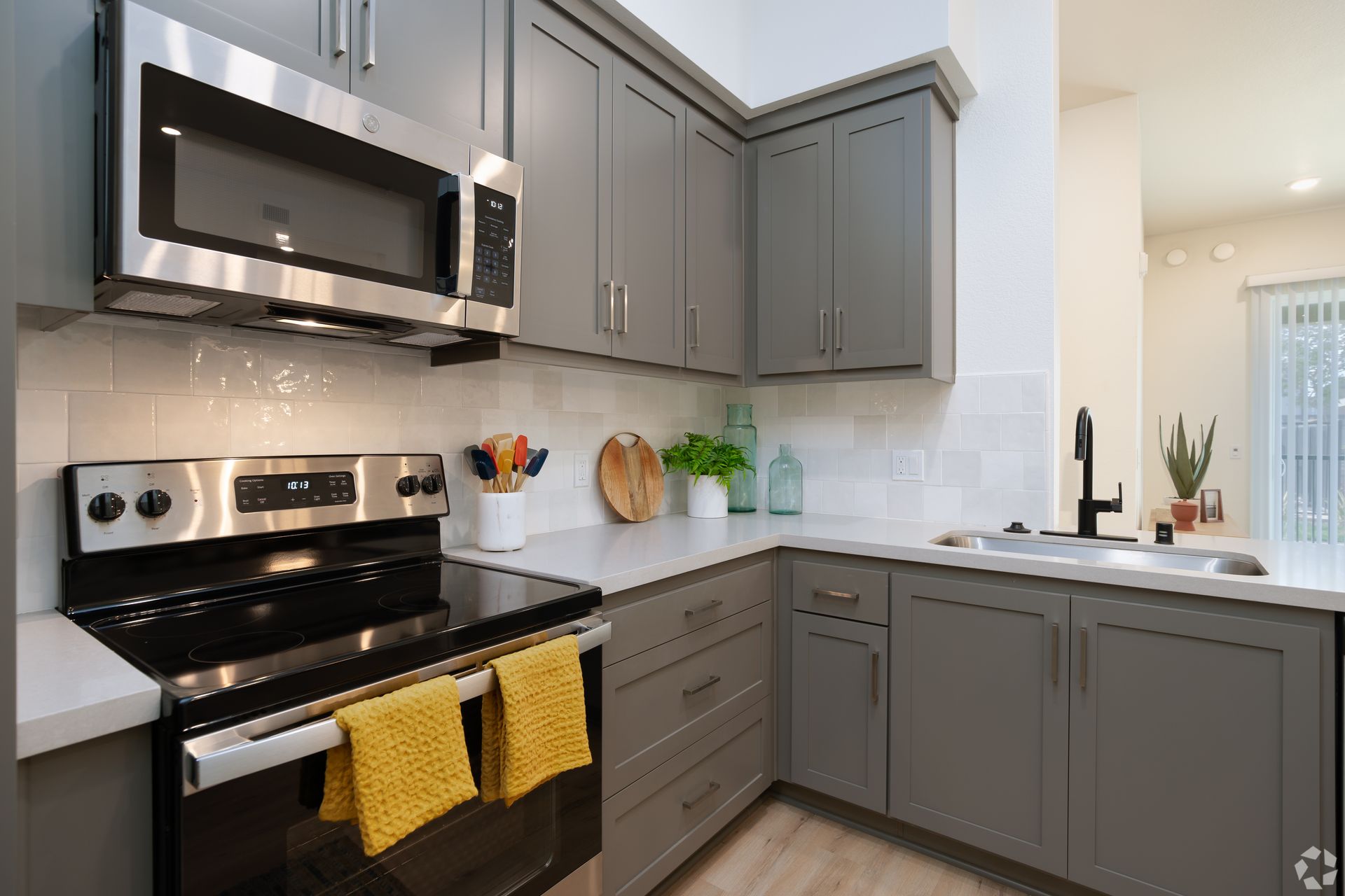 Modern kitchen with gray cabinets, stainless steel appliances, and white countertops.