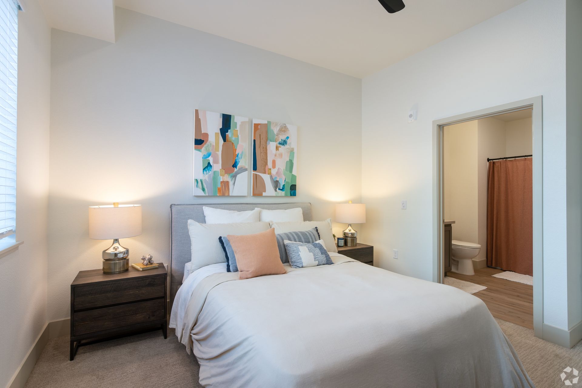Bedroom with bed, nightstands, abstract art, and doorway to bathroom. Neutral color palette.