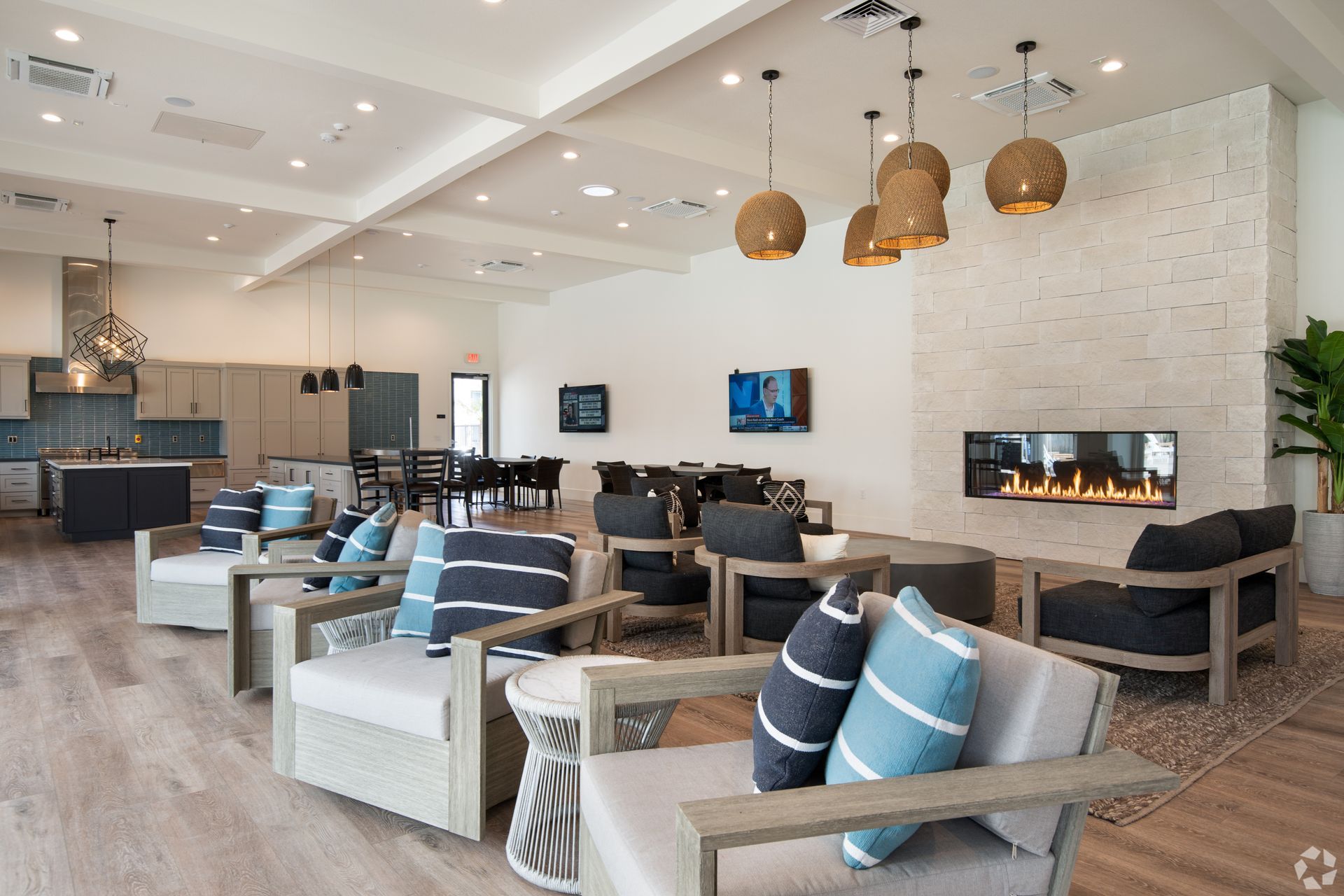 Spacious lounge area with neutral tones, several armchairs, fireplace, and kitchen in the background.