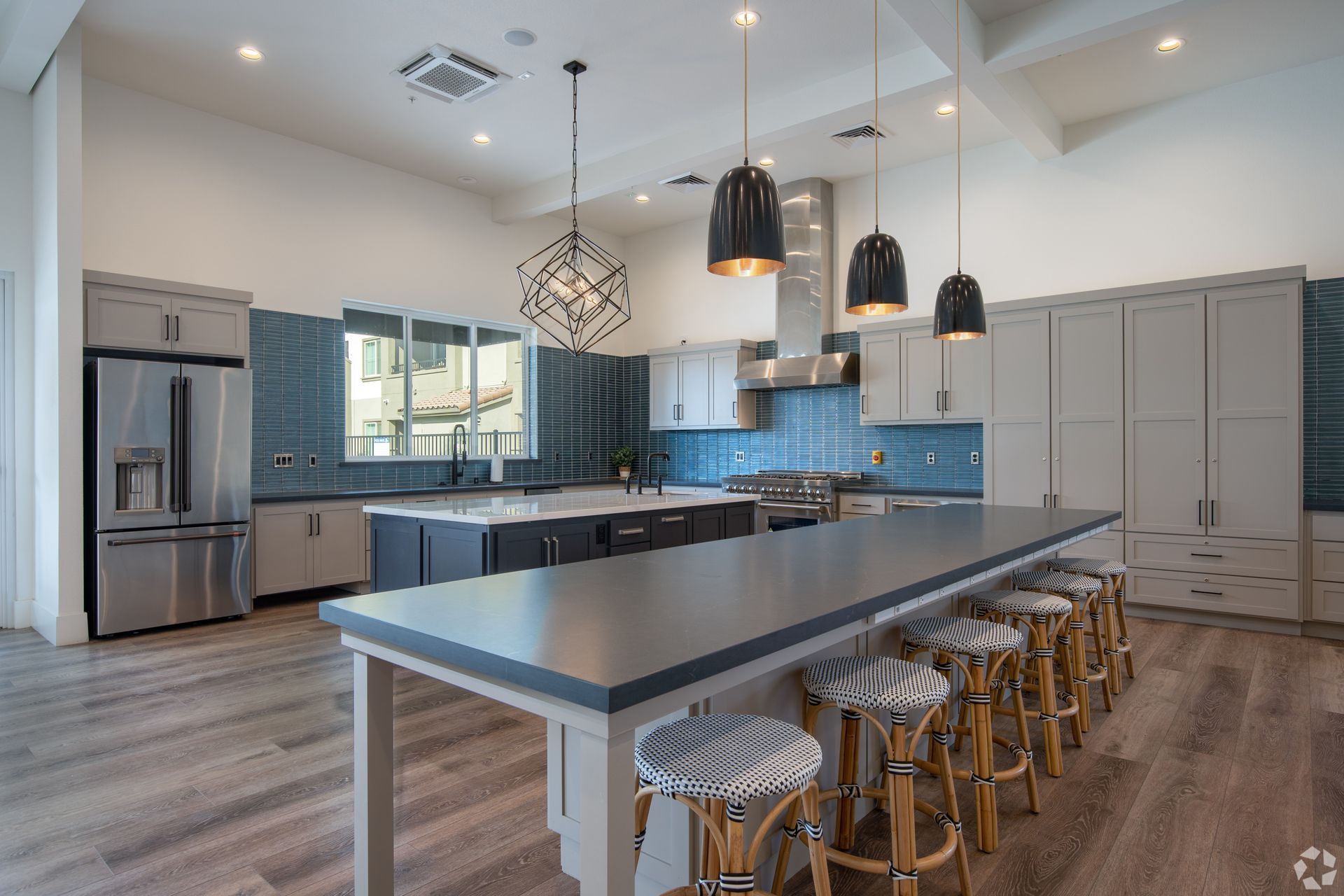 Spacious modern kitchen with island seating, blue tile backsplash, stainless steel appliances, and wood floors.