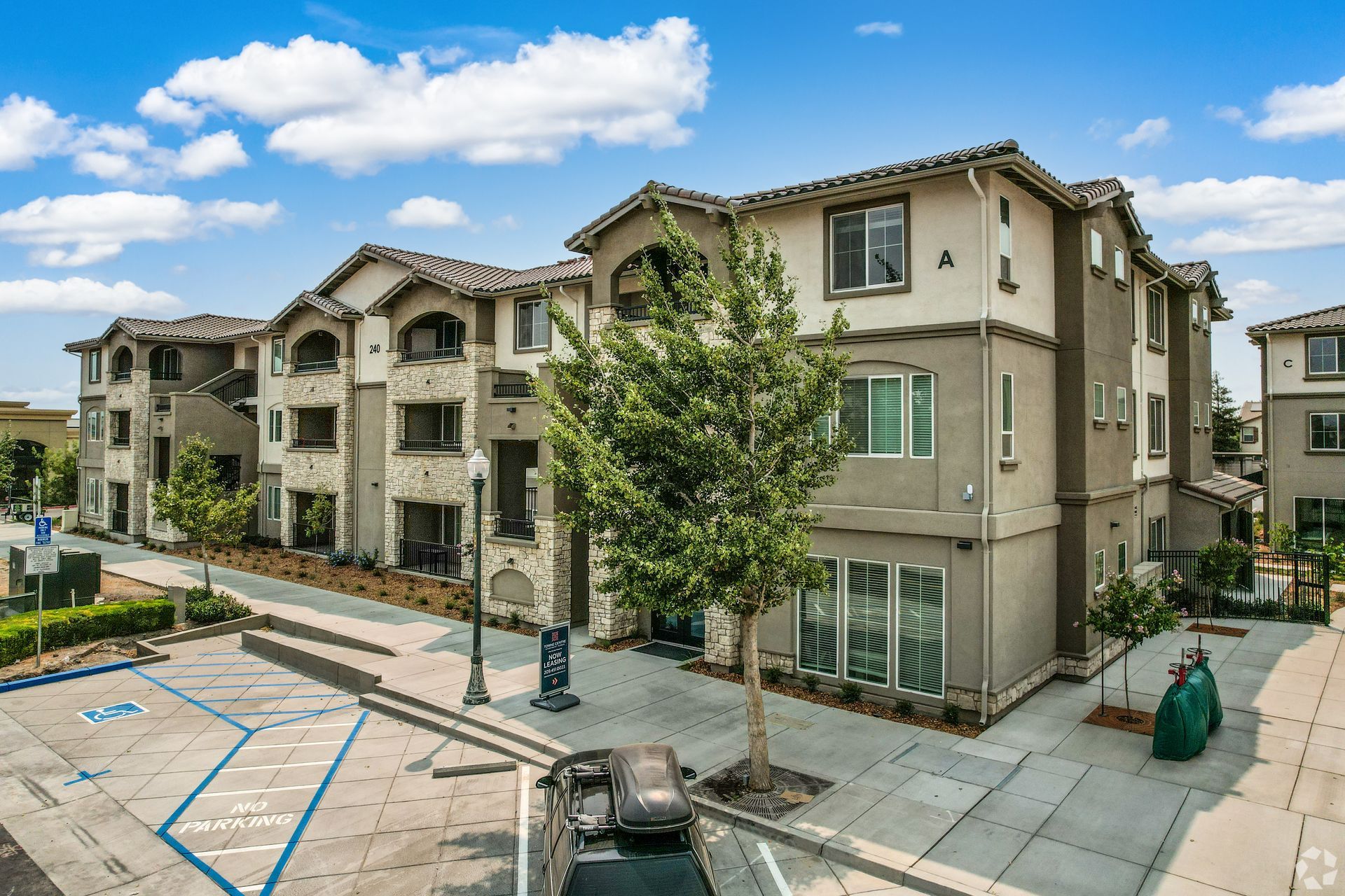 Apartment complex exterior with beige stucco, tiled roof, and a blue sky.