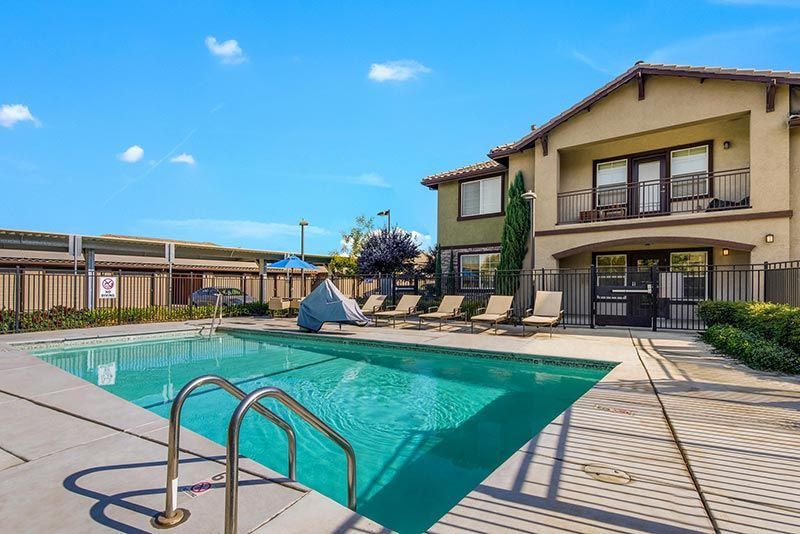 Swimming pool outside a two-story building on a sunny day. Lounge chairs sit by the pool.